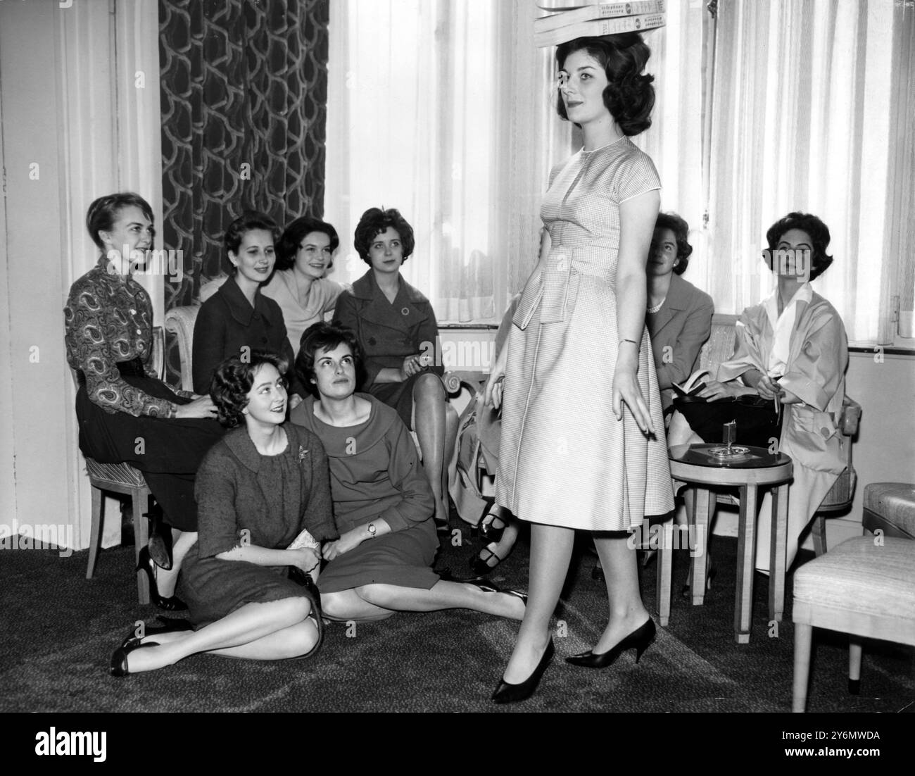 Virginia Lyon fa un passo maestoso con elenchi telefonici bilanciati sulla sua testa mentre pratica la deportazione al Berkely Hotel, Piccadilly, Londra. A guardare ci sono alcune delle altre debs che parteciperanno con lei al Debutantes' Dress Show. 9 aprile 1959 Foto Stock
