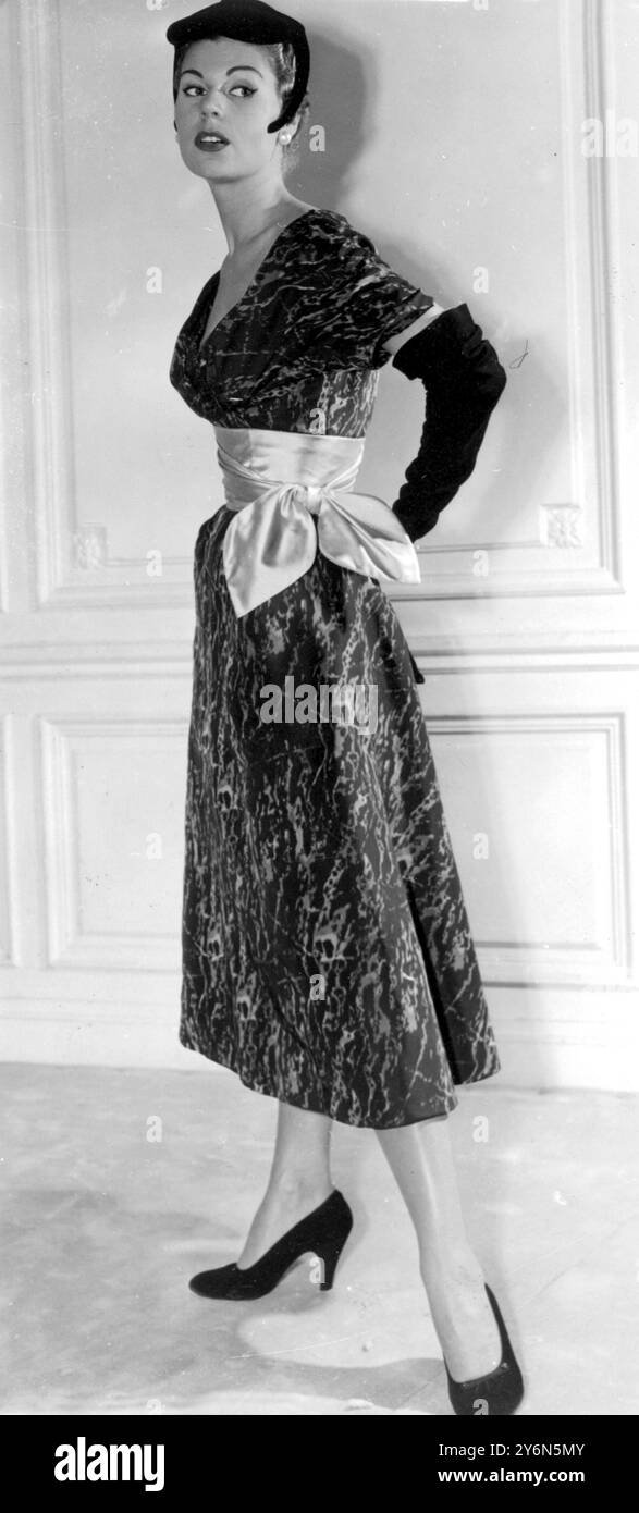 Parigi: Per l'ora del cocktail e l'abbigliamento serale informale generale Jacque Fath presenta questa nuova nota sia in tessuto che in linea. Il tessuto è un ottomano stampato con motivi in marmo - verde scuro con sfumature rosa. La linea sfoggia una consistenza contenuta nella gonna, un corpetto morbido drappeggiato e un effetto vita alta, grazie alla cintura profonda in raso verde nilo. Il tamburello in velluto nero piatto presenta "credenze" che scendono fino alla guancia. 28 agosto 1953 Foto Stock