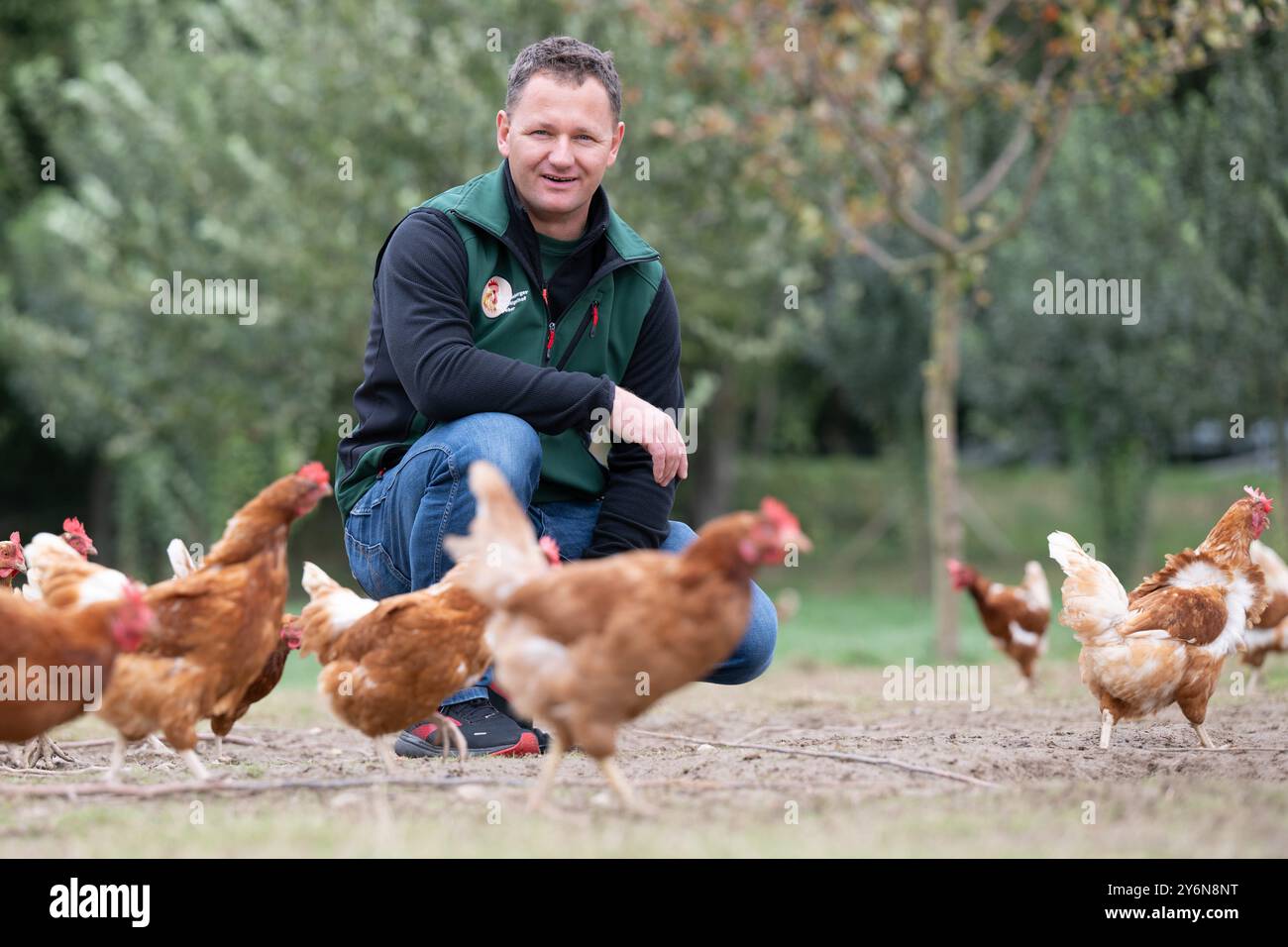 26 settembre 2024, Sassonia, Schönberg: Christian Weber, allevatore di animali, siede accanto alle sue galline ovaiole biologiche nella fattoria biologica Weber. L'azienda agricola biologica è stata premiata al primo posto nel concorso statale "zootecnia rispettosa degli animali e rispettosa dell'ambiente 2023/2024 in Sassonia" nella categoria allevamento di bovini/suini e pollame. Foto: Sebastian Kahnert/dpa/ZB Foto Stock