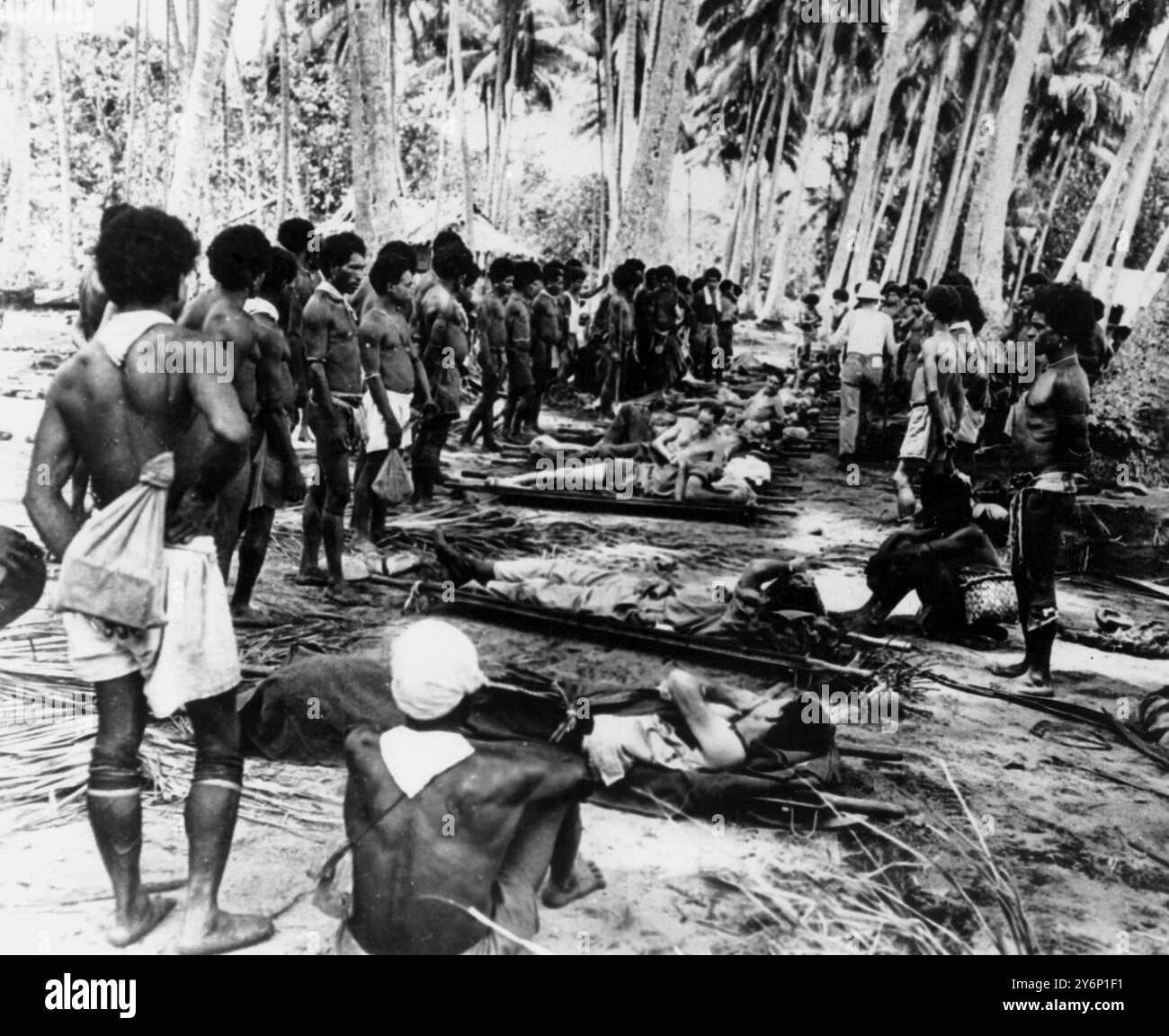 I portatori di barella nativi riposano all'ombra di un Coconut Grove mentre loro e i soldati americani feriti che trasportano dal fronte a Buna, nuova Guinea, cogliono l'occasione per rilassarsi. I feriti stanno andando agli ospedali sul retro. Pacifico 10 febbraio 1943 Foto Stock