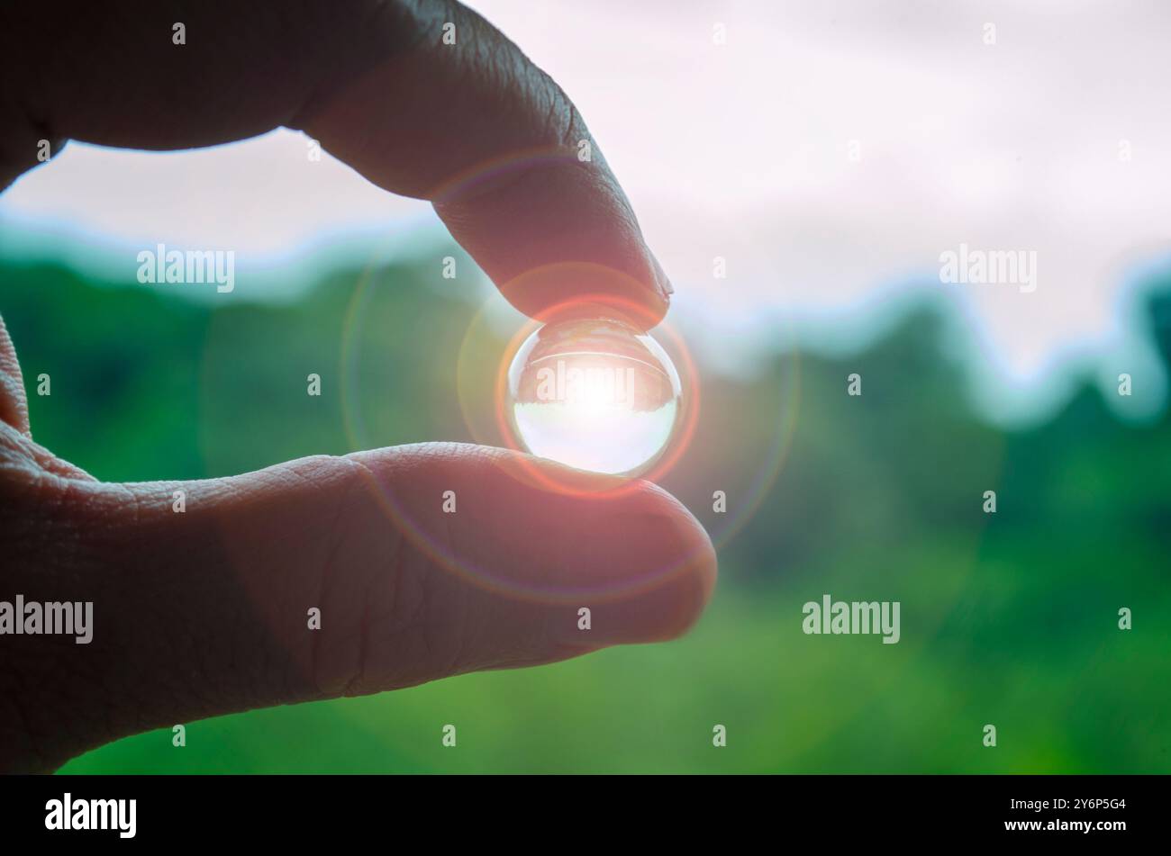 Mano che regge un marmo brillante con sfondo naturale sfocato. Foto Stock