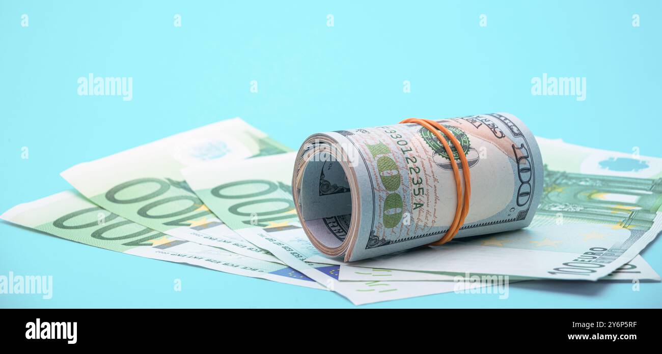 Una pila di dollari arrotolata è circondata da banconote da cento euro che simboleggiano la diversità finanziaria e l'economia globale. Foto Stock