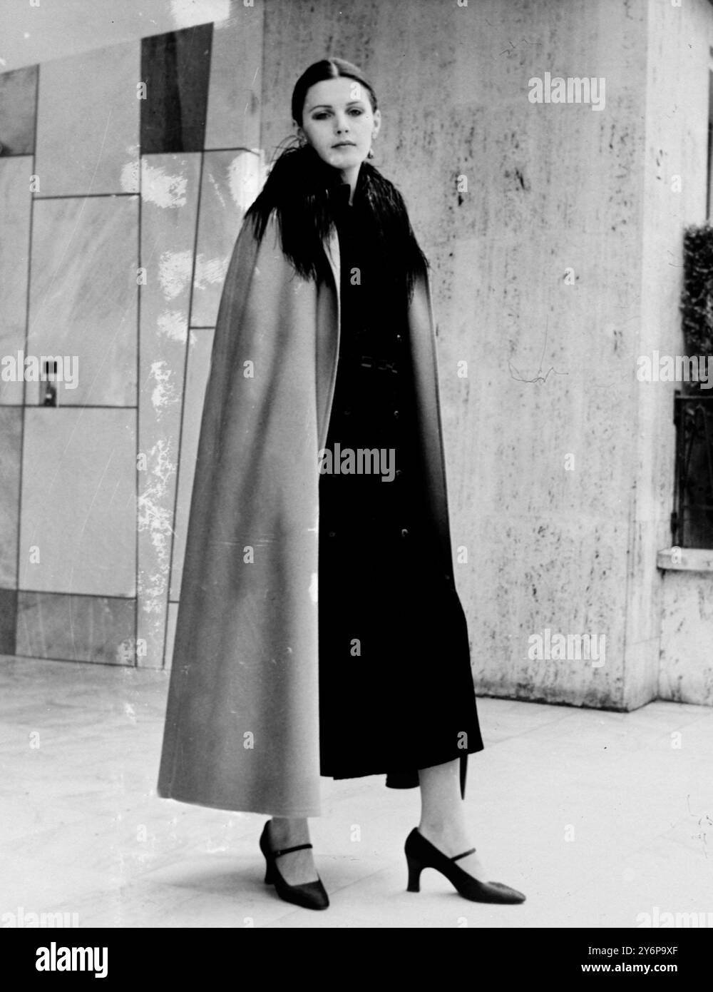 Parigi : tutti gli abiti da sera di Yves Saint Laurent sono perfetti per la gonna lunga . Qui usa un panno di raso in un colore che reintegra in alta moda - bois de Robe (palissandro) per un mantello girevole a tutta lunghezza con un piccolo colletto in piuma nera su un abito reed-slim in velluto stampato nero con doppia chiusura sul davanti . 7 agosto 1969 Foto Stock