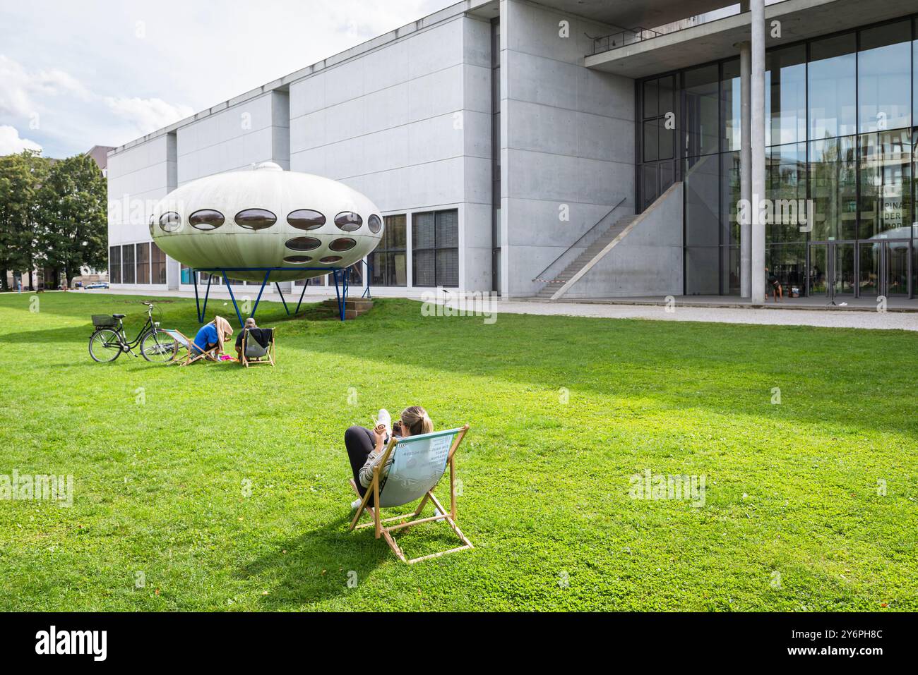 Persone sedute su sdraio sul prato di fronte alla Pinakothek der moderne e all'installazione artistica futuro House di Matti Suuronen, Monaco di Baviera Foto Stock