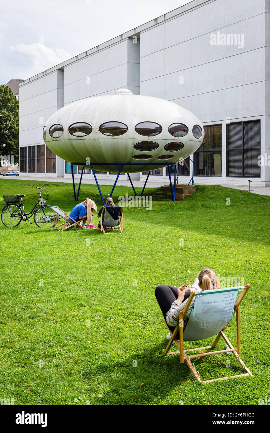Persone sedute su sdraio sul prato di fronte alla Pinakothek der moderne e all'installazione artistica futuro House di Matti Suuronen, Monaco di Baviera Foto Stock