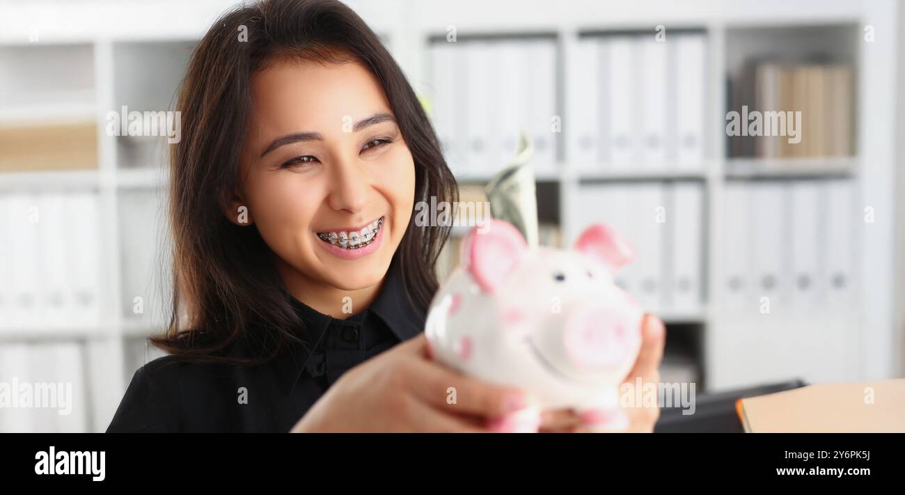 Bella ridendo giovane donna che tiene piggybank con banconota in esso Foto Stock