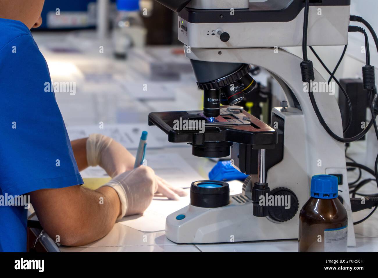 Donna scienziata in laboratorio universitario che lavora con il microscopio e scrive appunti Foto Stock