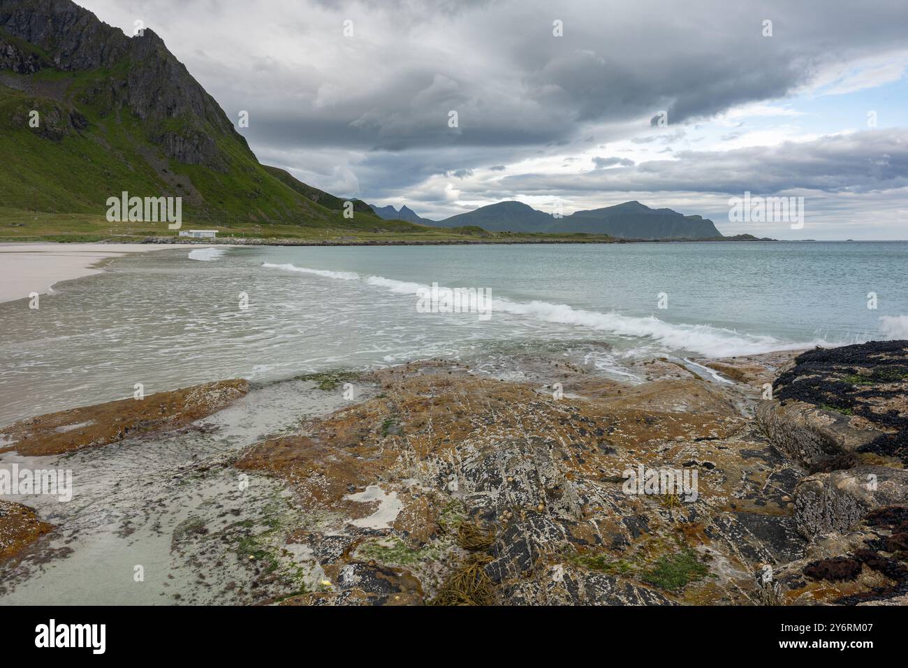 Spiaggia sabbiosa con pietre e montagne sullo sfondo nuvoloso, Lofoten Norvegia Foto Stock