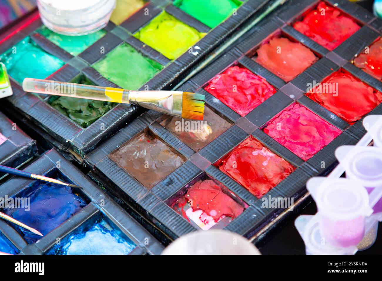 Una bellissima tavolozza piena di acquerelli vivaci e una spazzola appoggiata sulla parte superiore Foto Stock