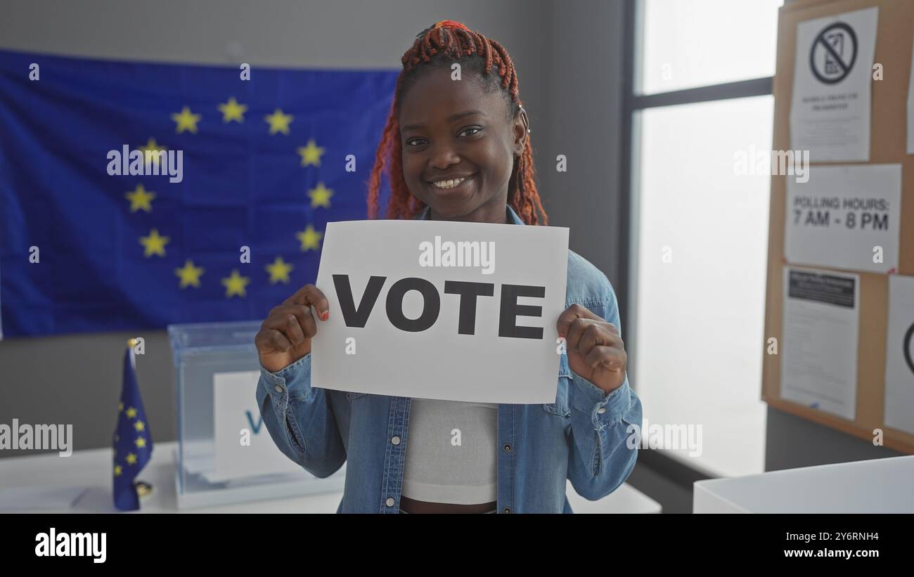 Giovane donna africana sorridente con un cartello di "voto” in una struttura di voto europea con sfondo bandiera ue Foto Stock