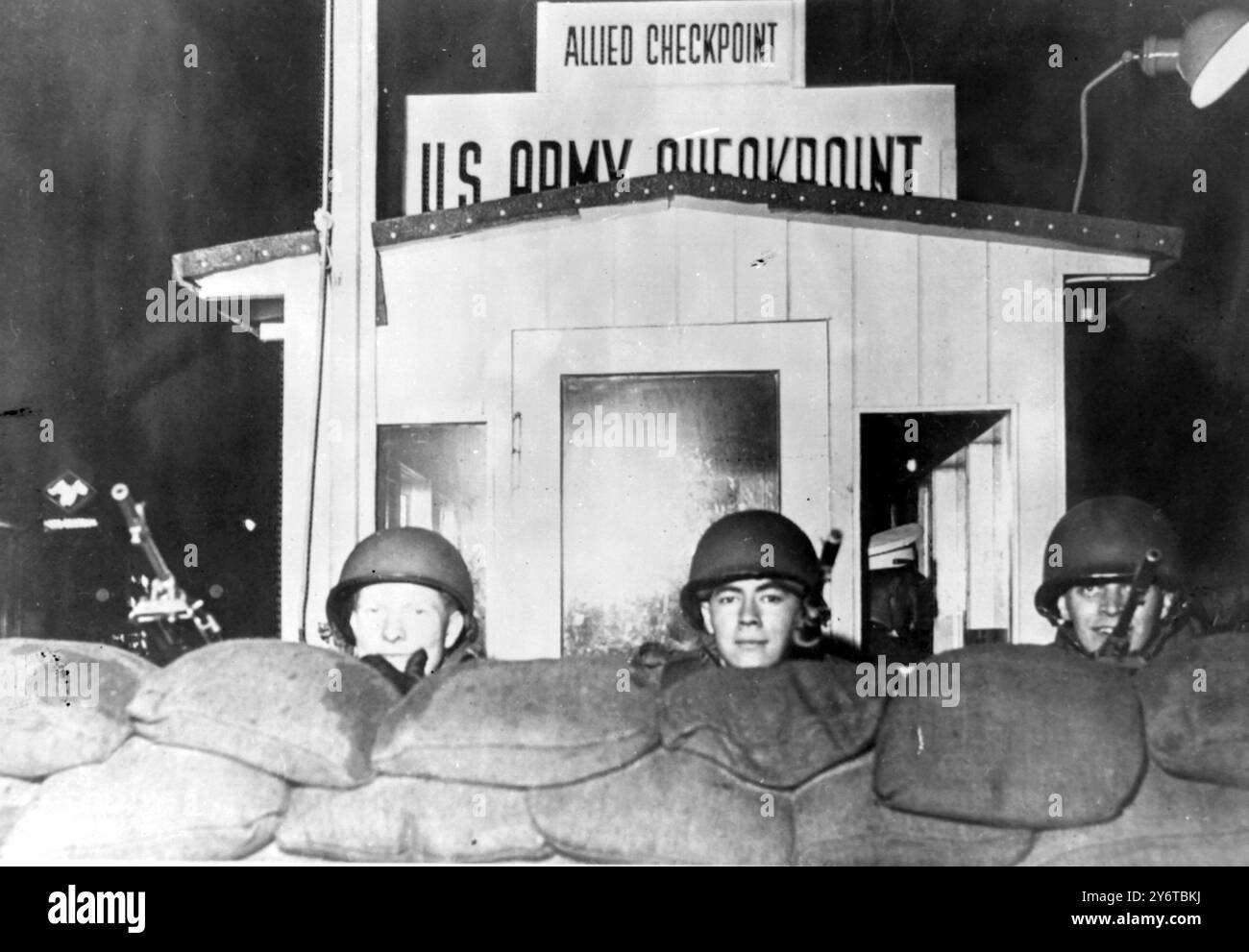 Le truppe armate degli Stati Uniti con elmetto d'acciaio osservano da dietro una barricata di sacchi di sabbia al Checkpoint Charlie sulla Friedrichstrasse tra Berlino Est e Berlino Ovest mentre la polizia e le truppe della Germania Est hanno iniziato a rafforzare il muro e a restringere l'ingresso delle auto a Berlino Est ieri sera. Le truppe STATUNITENSI sono state spostate fino al checkpoint per rafforzare la polizia militare quando le autorità della Germania Est hanno iniziato a lavorare sul muro. 4 DICEMBRE 1961 Foto Stock