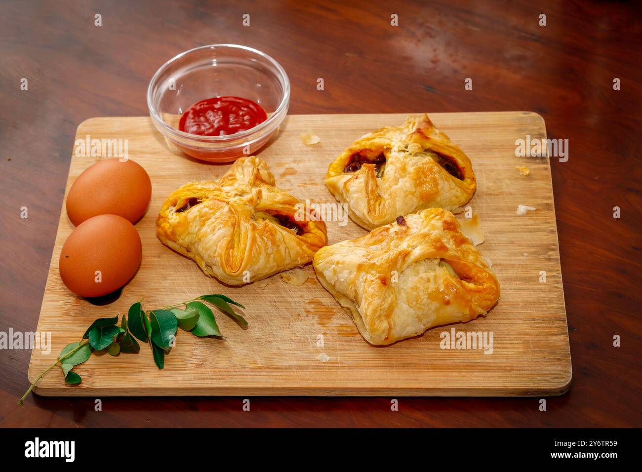 Primo piano immagine dei gustosi braccialetti d'uovo in stile Kerala con salsa di pomodoro, foglie di curry e uovo su tagliere. Sfondo in legno Foto Stock