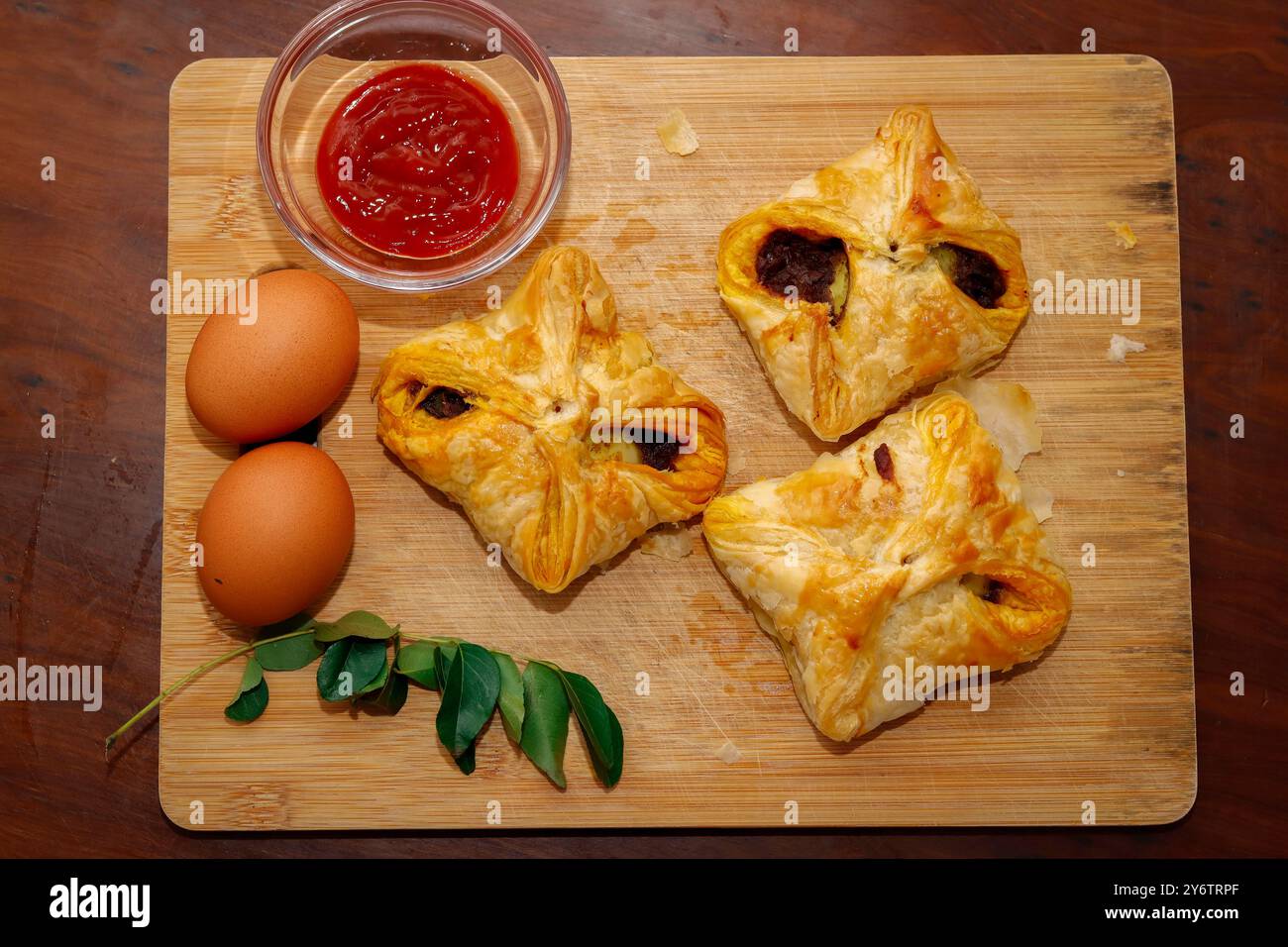 Primo piano immagine dei gustosi braccialetti d'uovo in stile Kerala con salsa di pomodoro, foglie di curry e uovo su tagliere. Sfondo in legno Foto Stock