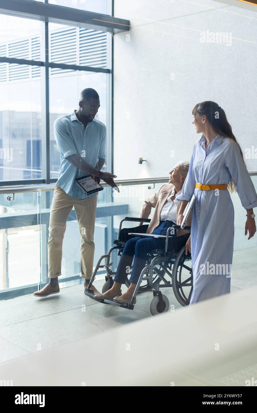 Assistere una donna anziana in sedia a rotelle, un uomo afroamericano e una donna che discutono delle indicazioni in casa Foto Stock