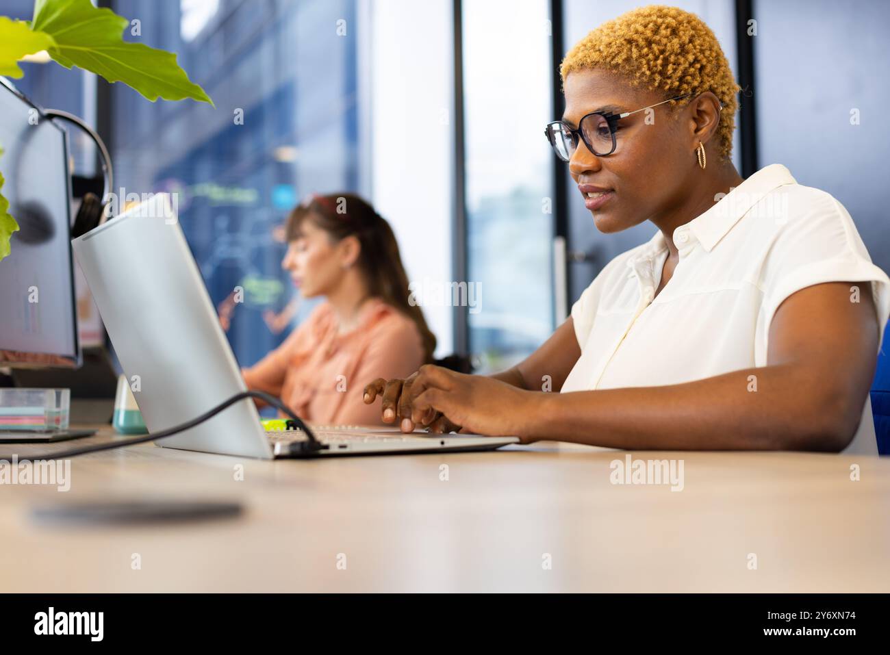 Lavora con un computer portatile, donna con occhiali che scrive alla scrivania in un ufficio moderno Foto Stock