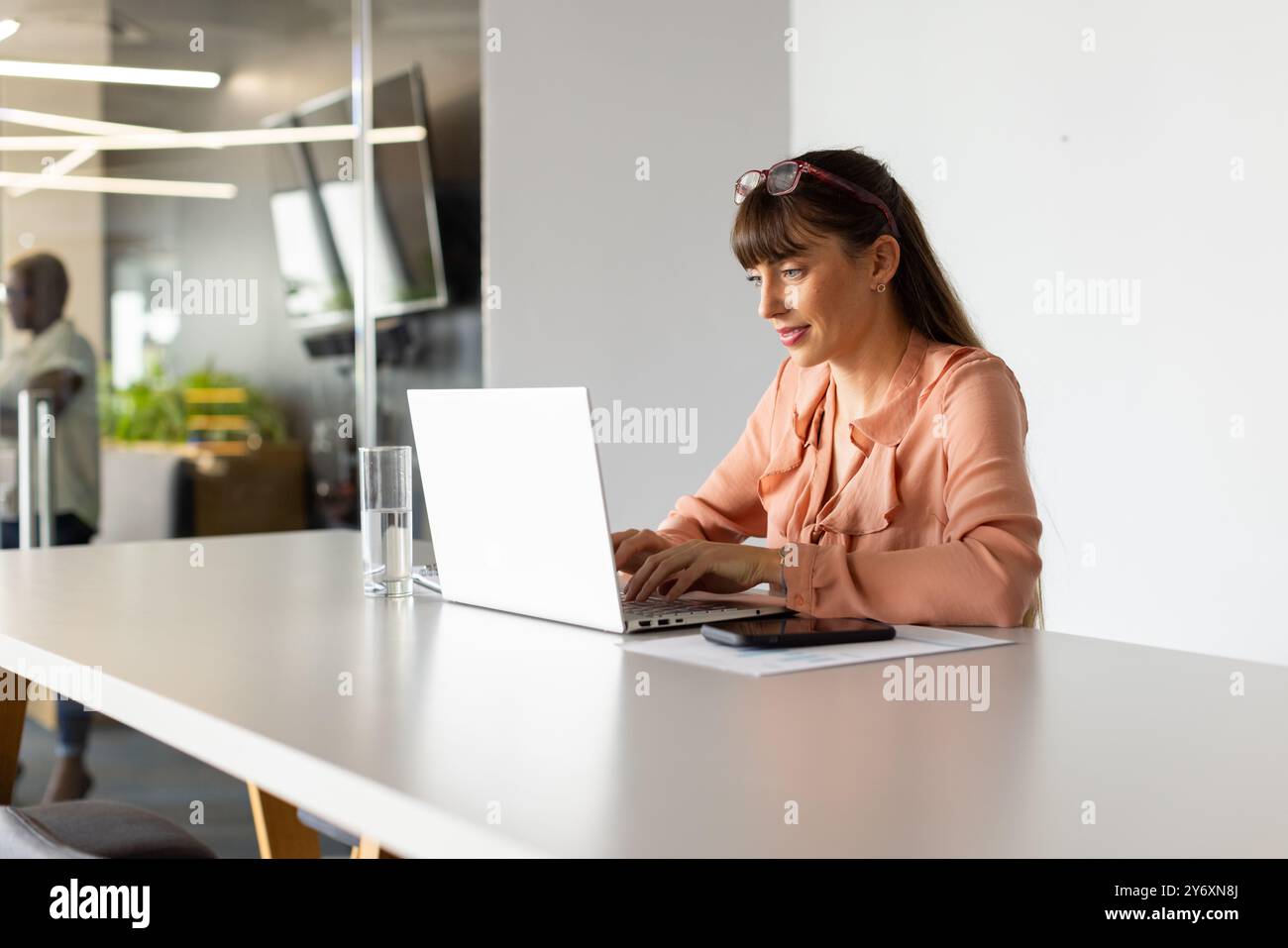 Digitazione su laptop, donna che lavora alla moderna scrivania con smartphone e vetro Foto Stock