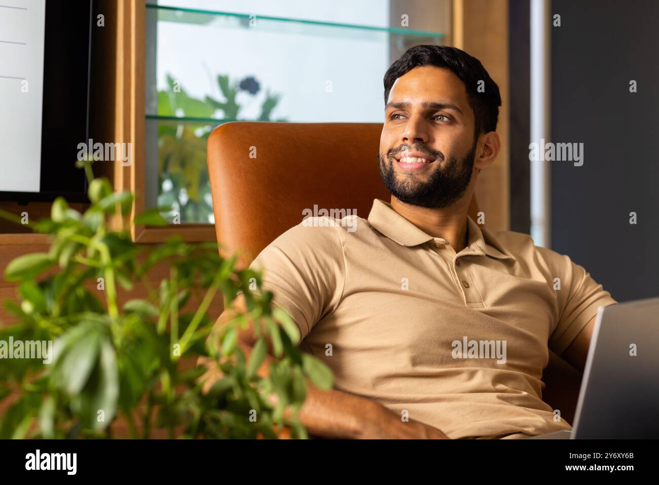 Uomo sorridente seduto su una sedia con un computer portatile, che guarda lontano dallo schermo Foto Stock