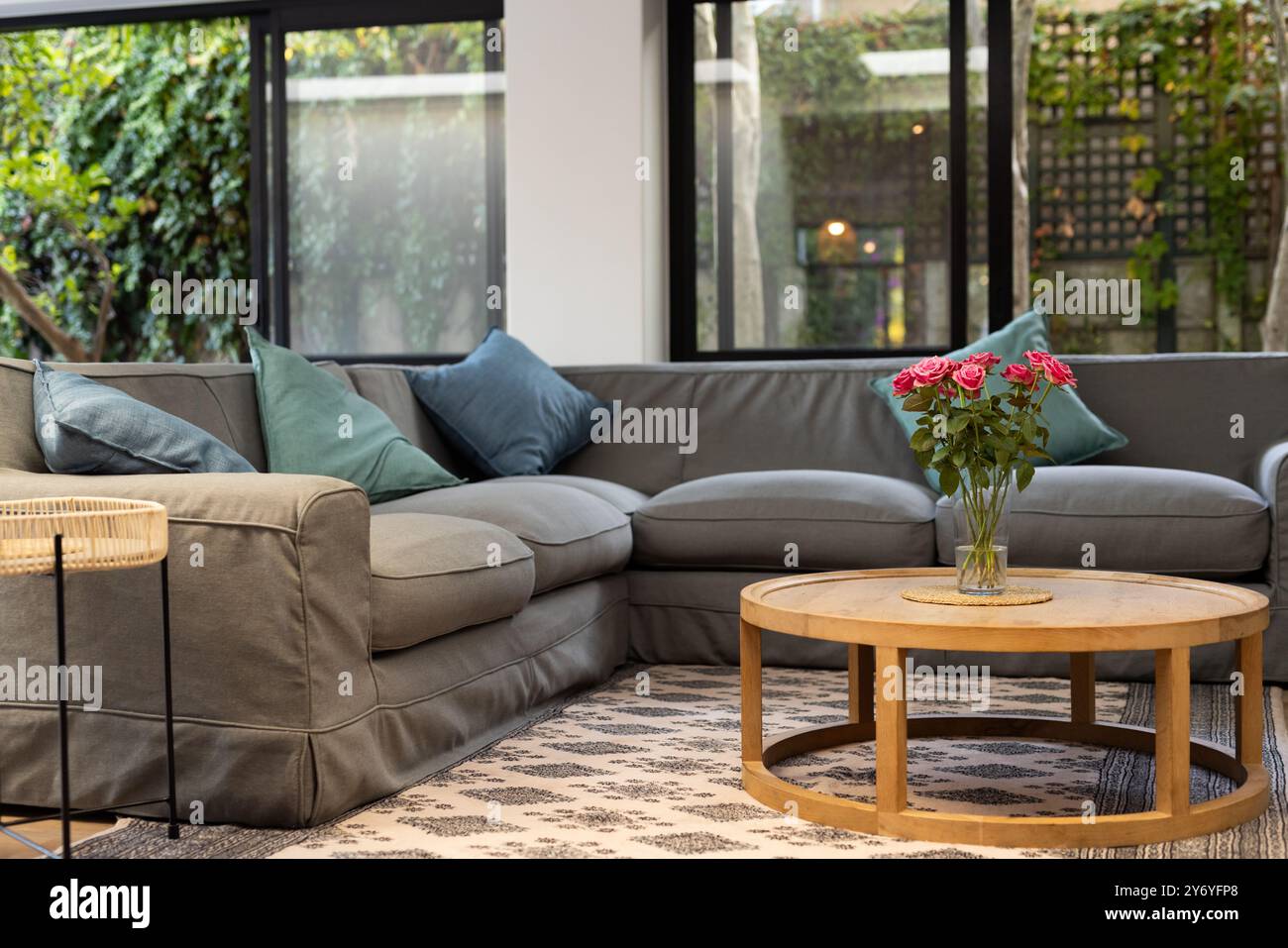 Soggiorno con accogliente divano componibile e tavolino rotondo in legno con fiori, spazio fotocopie, a casa Foto Stock