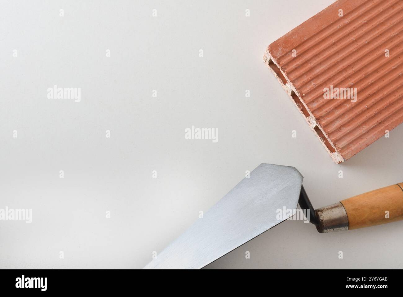 Cazzuola per muratura e costruzione con cazzuola in metallo con manico in legno e mattoni con tre fori arancioni isolati su sfondo bianco. Vista dall'alto. Foto Stock