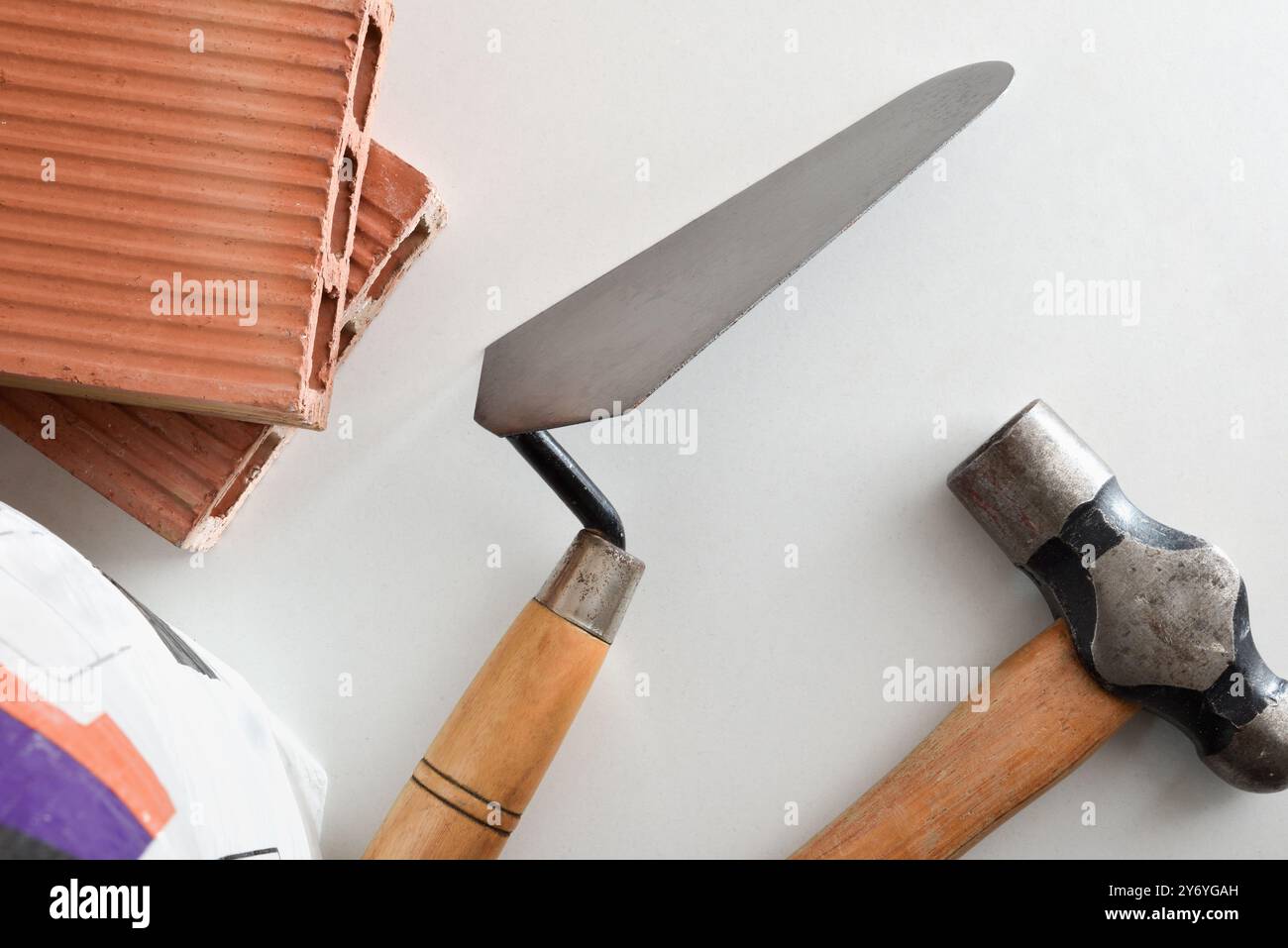 utensili e materiali per muratore come cazzuola, martello, mattoni e sacchetti di cemento su sfondo bianco. Vista dall'alto. Foto Stock