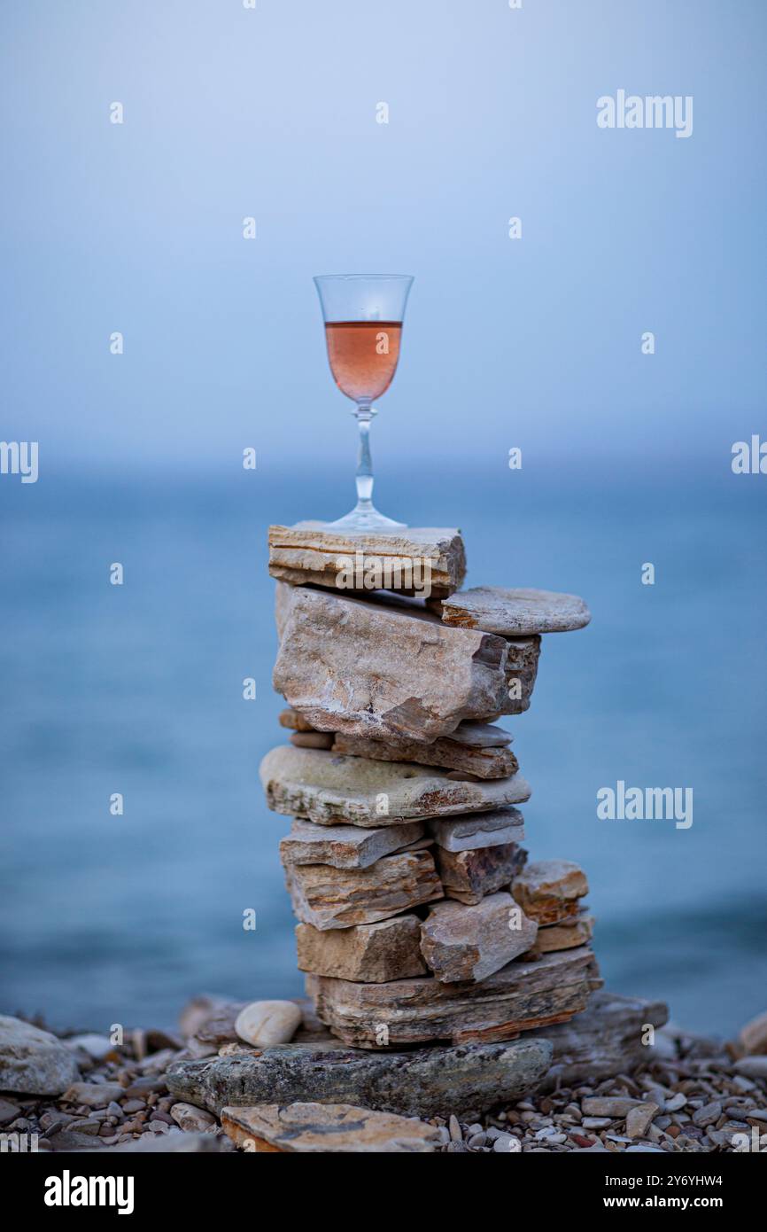 Bicchiere di vino rosa sui cairns di pietra sullo sfondo del mare sfocato Foto Stock