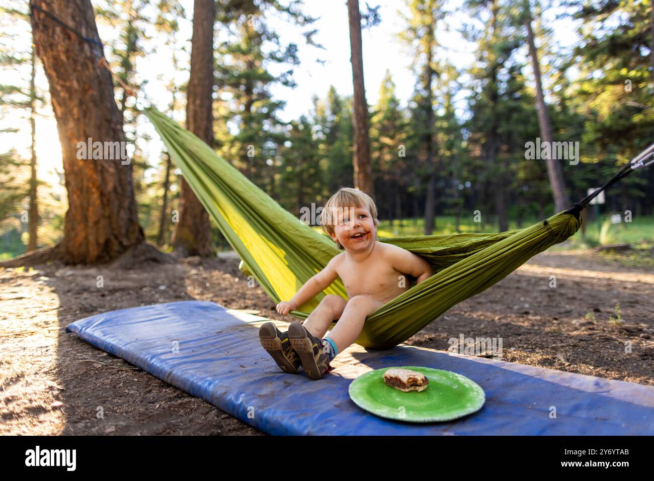 Un bambino sorride mentre gioca su un'amaca mentre campeggia. Foto Stock