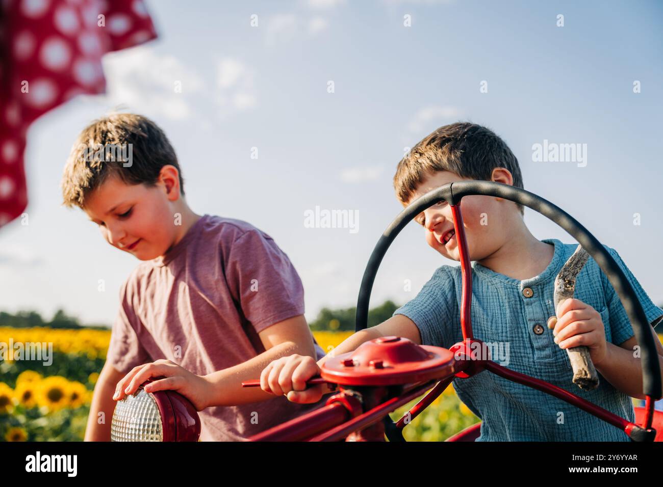 Due ragazzi che giocano su un trattore rosso in un campo di girasole Foto Stock