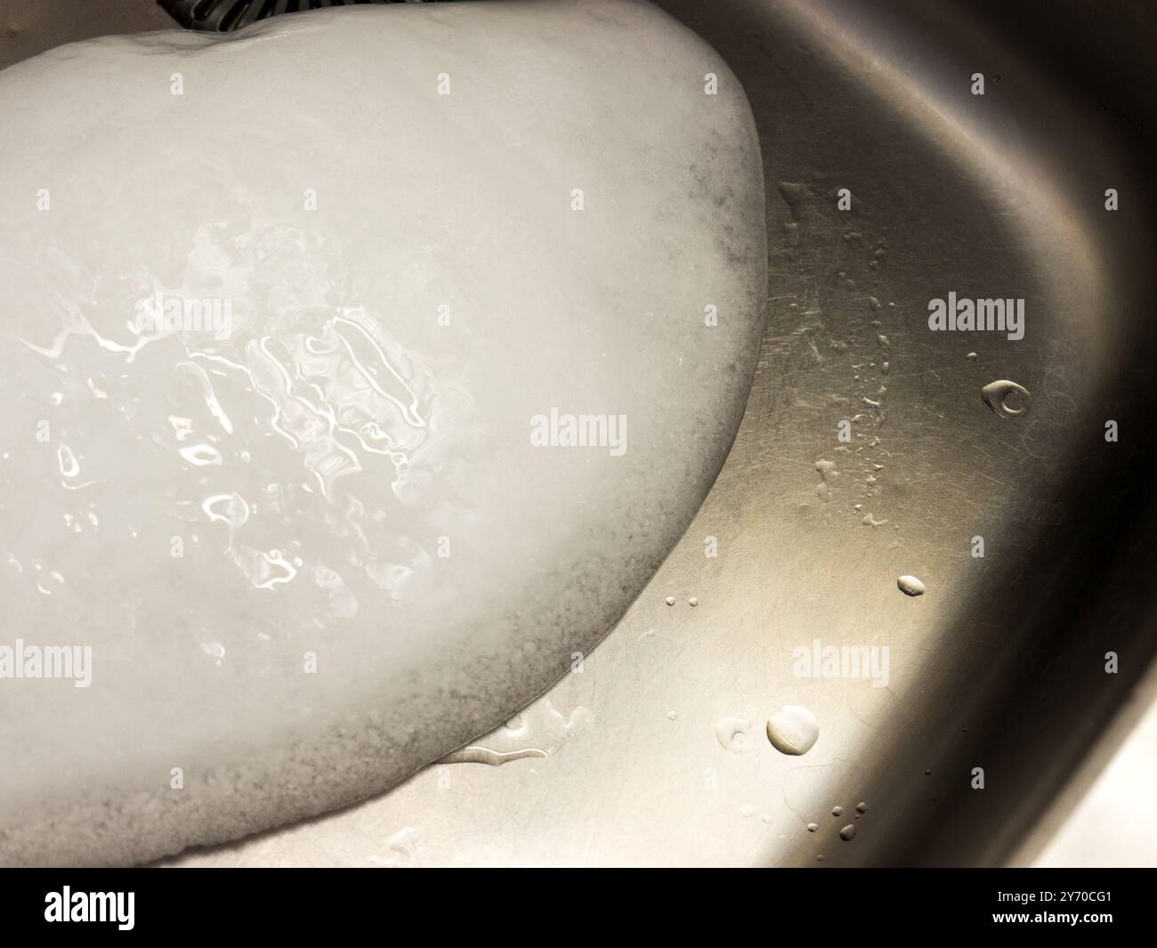 Un pezzo di ghiaccio in un lavandino di metallo. Foto Stock