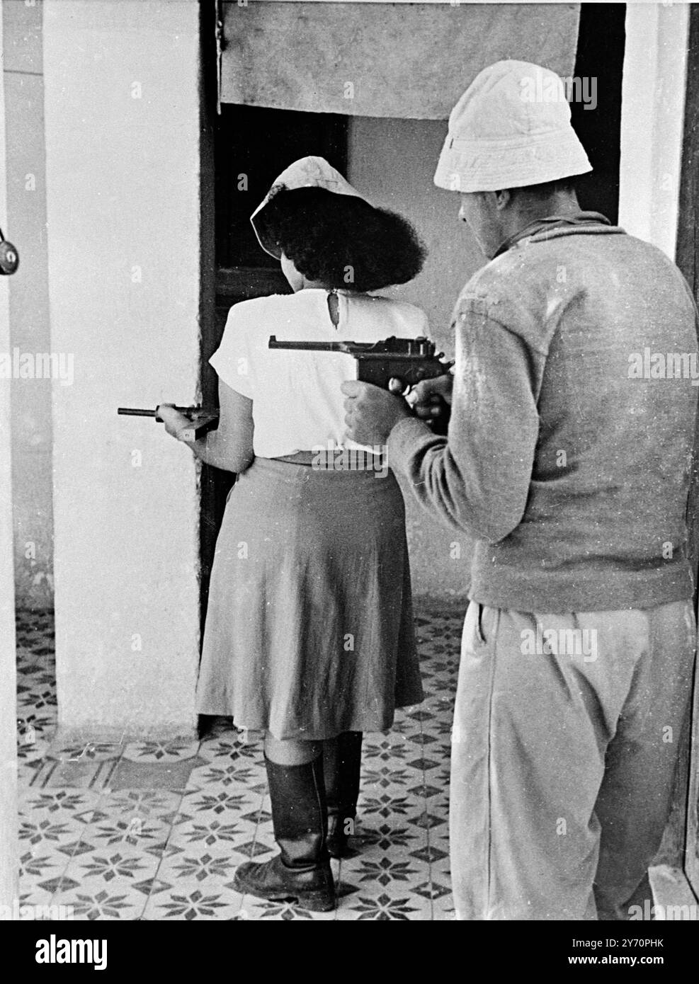 L'HAGANAH ILLEGALE GUARDIA FURTIVAMENTE IL CONFINE TRA TEL AVIV e JAFFA i membri armati dell'Haganah sorvegliano i tetti, i balconi e sono pronti a cedere da dietro le finestre chiuse del confine tra Tel Aviv e Jaffa. Mentre trasportano armi illegali, svolgono il loro compito in modo furtivo. SPETTACOLI FOTOGRAFICI: Una donna membro di Haganah e un membro maschio stanno in una casa pronta a sparare attraverso una finestra che si apre sul confine di Tel Aviv Jaffa. 16 dicembre 1947 Foto Stock