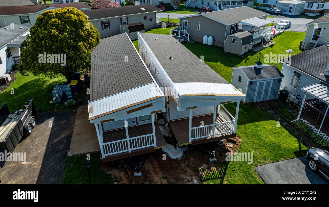 La vista aerea mostra le case mobili costruite lungo una strada tranquilla, circondate da prati e alberi ben tenuti. Il sole diffonde una luce calda, evidenziando la disposizione e la struttura curate. Foto Stock