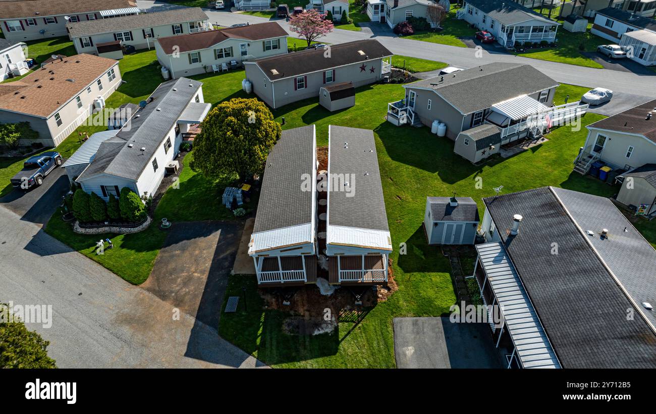 La vista aerea mostra le case mobili costruite lungo una strada tranquilla, circondate da prati e alberi ben tenuti. Il sole diffonde una luce calda, evidenziando la disposizione e la struttura curate. Foto Stock