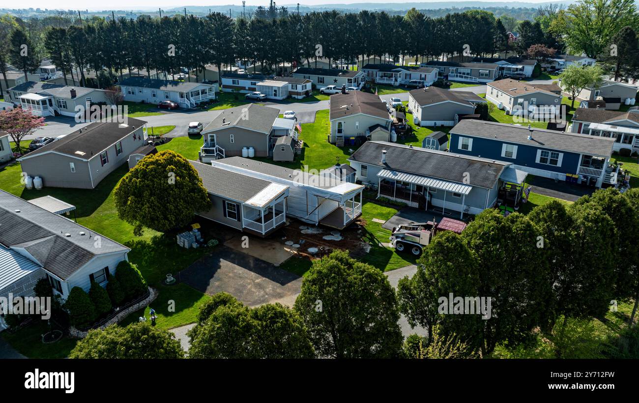 La vista aerea mostra le case mobili costruite lungo una strada tranquilla, circondate da prati e alberi ben tenuti. Il sole diffonde una luce calda, evidenziando la disposizione e la struttura curate. Foto Stock