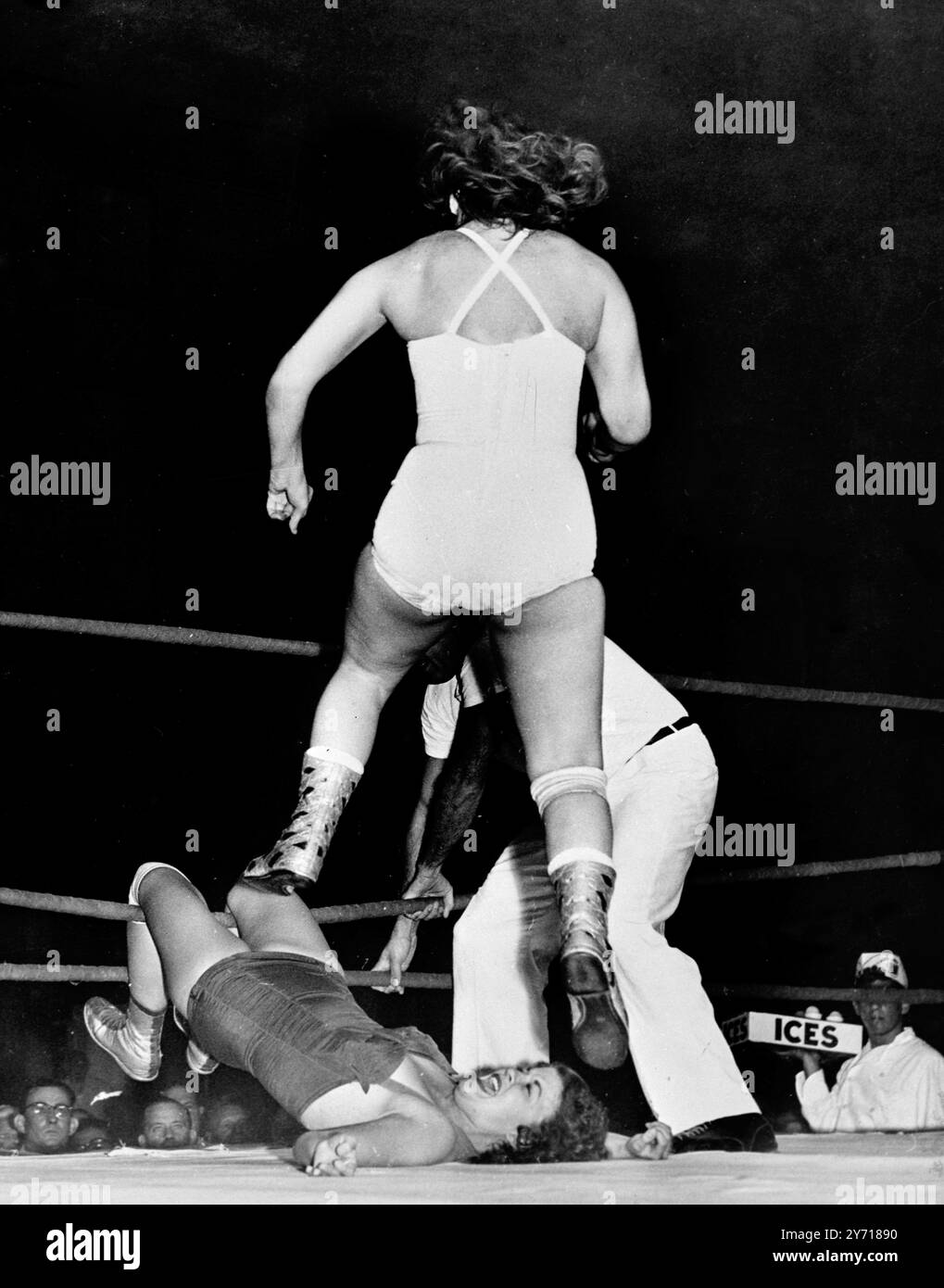 Un venditore continua casualmente a vendere il suo gelato mentre la lottatrice Betty Larkin salta sullo stomaco di Jerry Ford durante una gara di casa a Miami , Florida , USA . Betty aveva messo i piedi di Jerry tra le corde per tenerla messa e saltò su di lei tre volte , scavando gli stivali nel suo corpo ogni volta , prima che l' arbitro la prendesse mentre stava entrando e la gettasse di nuovo sul tappeto . Poi liberò Jerry , che gridava terrore , dalle corde . 22 settembre 1954 Foto Stock