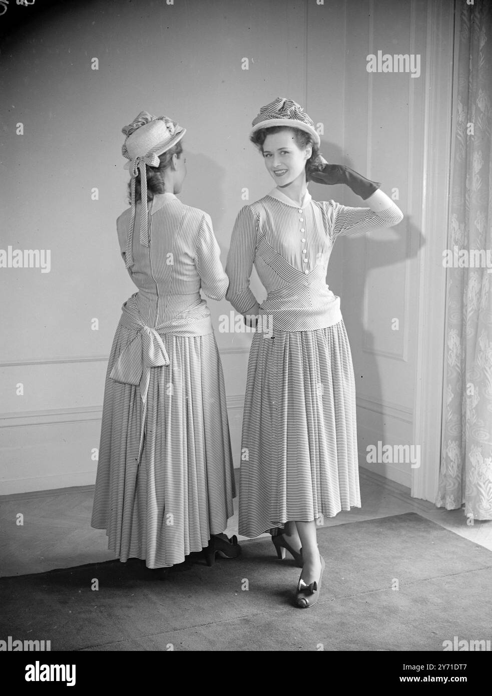 DOPPIAMENTE DELIZIOSA Una nuova idea nella presentazione della moda è stata ideata da JOY RICARDO , che permette alla sua clientela di vedere entrambi i lati di una discussione a favore dello stile. Due manichini modellano la stessa camicia e lo spettatore vede l'impressione generale dalla parte posteriore a quella anteriore. Se e' un uomo, puo' ancora avere un secondo sguardo. L'IMMAGINE MOSTRA:- Un grazioso modello di influenza edoardiana- in marina e rayon filato bianco. con colletto bianco. Il drappo d'anca striato si avvolge in un fiocco di trambusto sul retro, mentre il telo si apre per la stiratura. La gonna intera mostra la nuova linea pavone, immersa nella schiena, chiamata "PASTORALE", che si trova a metà Foto Stock