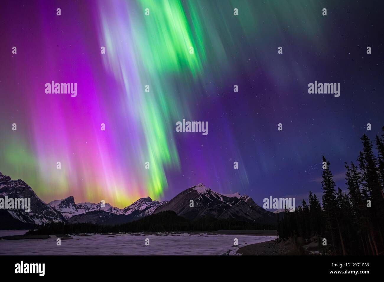 Aurora boreale che riempie il cielo di vibranti colori viola e verde su una catena montuosa innevata Foto Stock