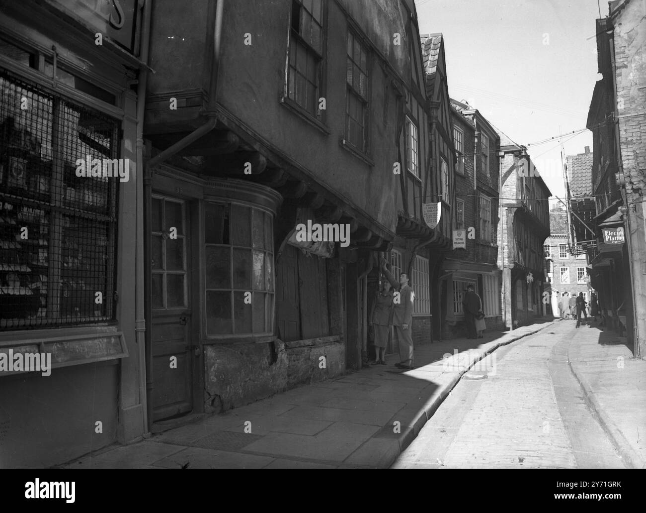 La strada pendente di York. Le case e i negozi che si aprono in avanti sono una caratteristica delle Shambles, una parte di York che è effettivamente menzionata a Domesday. Un tempo centro di macellazione, il caos è ora un centro di macellerie. I lavori di riparazione e conservazione sono in corso e si sta cercando seriamente di preservare il carattere della strada che in passato ha attirato così tanti visitatori. Alcuni dei gables sono così vicini che è effettivamente possibile stringere la mano da una finestra superiore con un vicino dall'altra parte della strada. 1952 Foto Stock