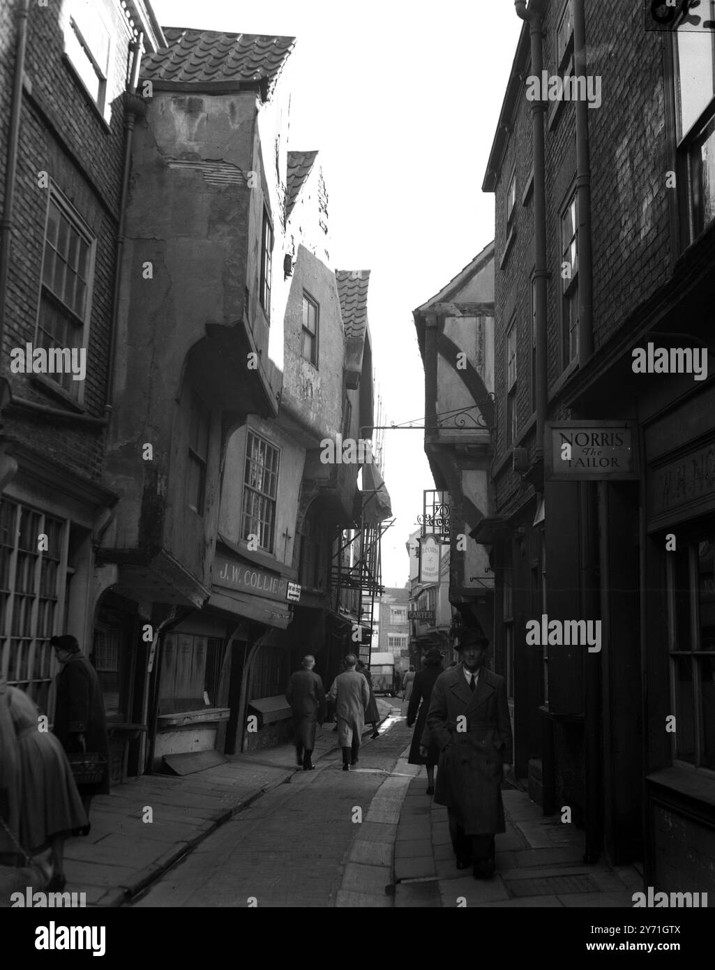 La strada pendente di York. Le case e i negozi che si aprono in avanti sono una caratteristica delle Shambles, una parte di York che è effettivamente menzionata a Domesday. Un tempo centro di macellazione, il caos è ora un centro di macellerie. I lavori di riparazione e conservazione sono in corso e si sta cercando seriamente di preservare il carattere della strada che in passato ha attirato così tanti visitatori. Alcuni dei gables sono così vicini che è effettivamente possibile stringere la mano da una finestra superiore con un vicino dall'altra parte della strada. 1952 Foto Stock