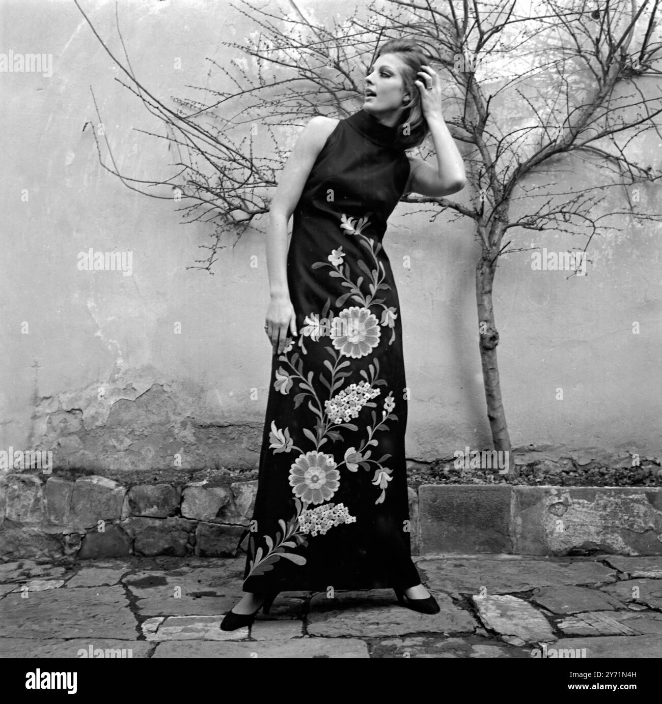 Abito da sera estivo in panama nero della Collezione Primavera / Estate 1965 di Gobo , di Firenze . L'abito presenta un ricamo a tutta lunghezza di fiori e foglie nei colori arancio, viola e verde sul davanti. Il vestito sottile e affusolato è senza maniche e abbraccia il collo , raccolto intorno alla vita , e quindi cade con delicata allentamento alle caviglie . L'abito trae la sua originalità dal ricamo caratterizzato da due fiori simili al sole e dona un aspetto broccato al modello. 20 gennaio 1965 Foto Stock