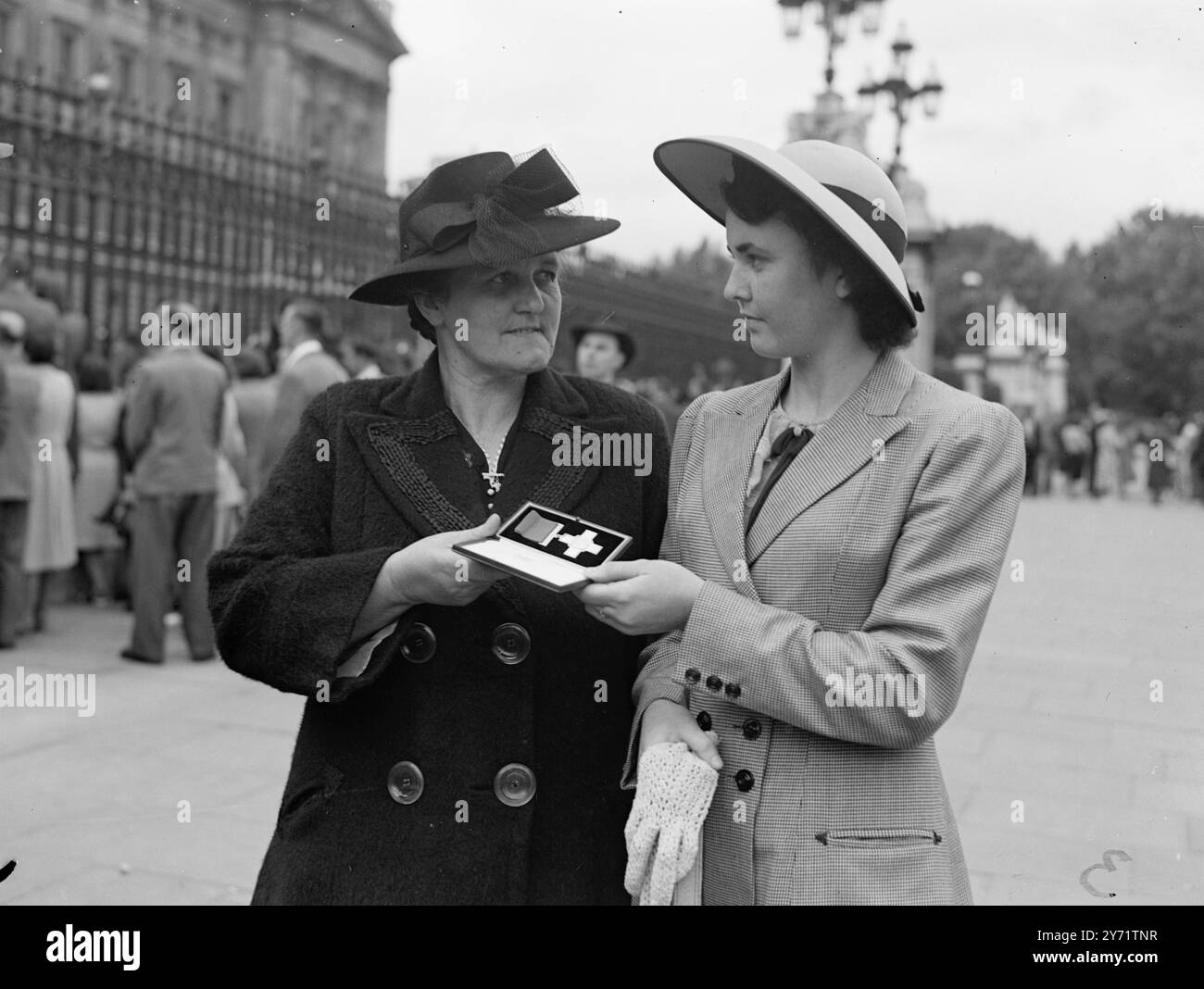 Sua Maestà il Re detiene l'investitura Mrs Rebecca Kelly (a sinistra), madre di Thomas Raymond Kelly, 19 anni, di Newry, Antrim, County Down, l'Irlanda, morta salvando la vita in mare, è stata insignita postumo della George Cross. La signora Kelly mostra il premio a sua figlia dopo l'investitura di sua Maestà il Re, oggi a Buckingham Palace. 20 luglio 1948 Foto Stock