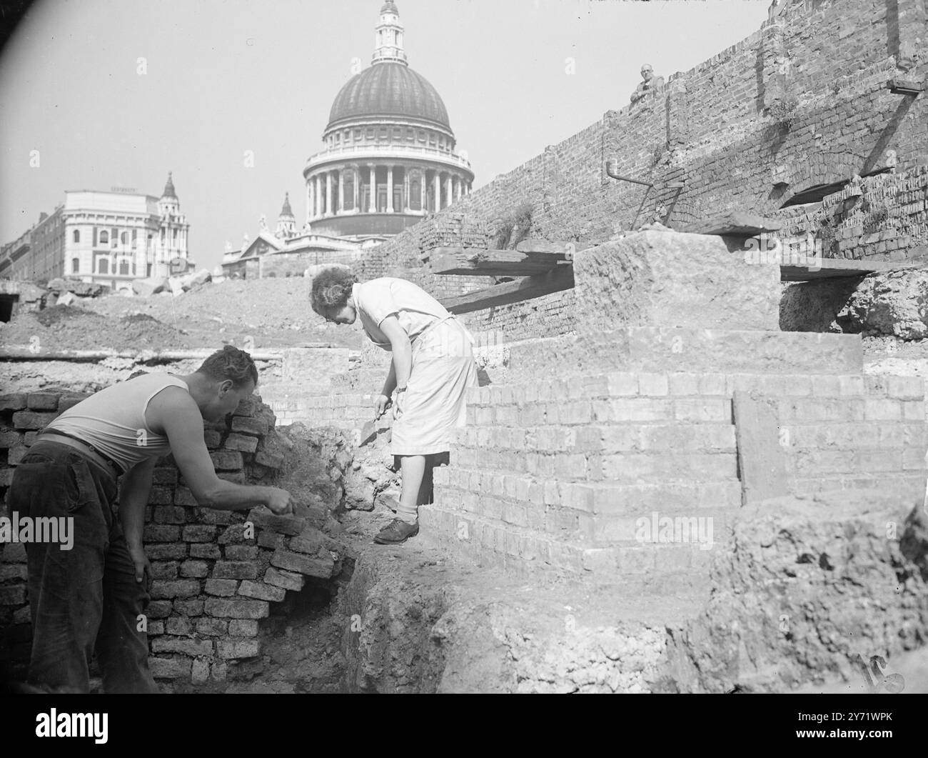 In cerca di una città. Tra le rovine bombardate della City di Londra, gli uomini sono impegnati a scavare nella speranza di trovare una città perduta quella dei Romani. Il sito principale - uno dei tre - si trova nella zona di Cannon Street - Queen Victoria Street, ad est di St Paul's, il centro della Londra romana. Nelle vicinanze sono già state rinvenute tracce di edifici romani, ma i lavori sono ostacolati dalle moderne fondamenta e dalle discariche medievali. Le immagini mostrano : il signor G R Faulkner e la signorina B J Harding, due operai volontari delle vacanze, che aiutano con gli scavi. La cupola della Cattedrale di San Paolo può essere vista nel bac Foto Stock