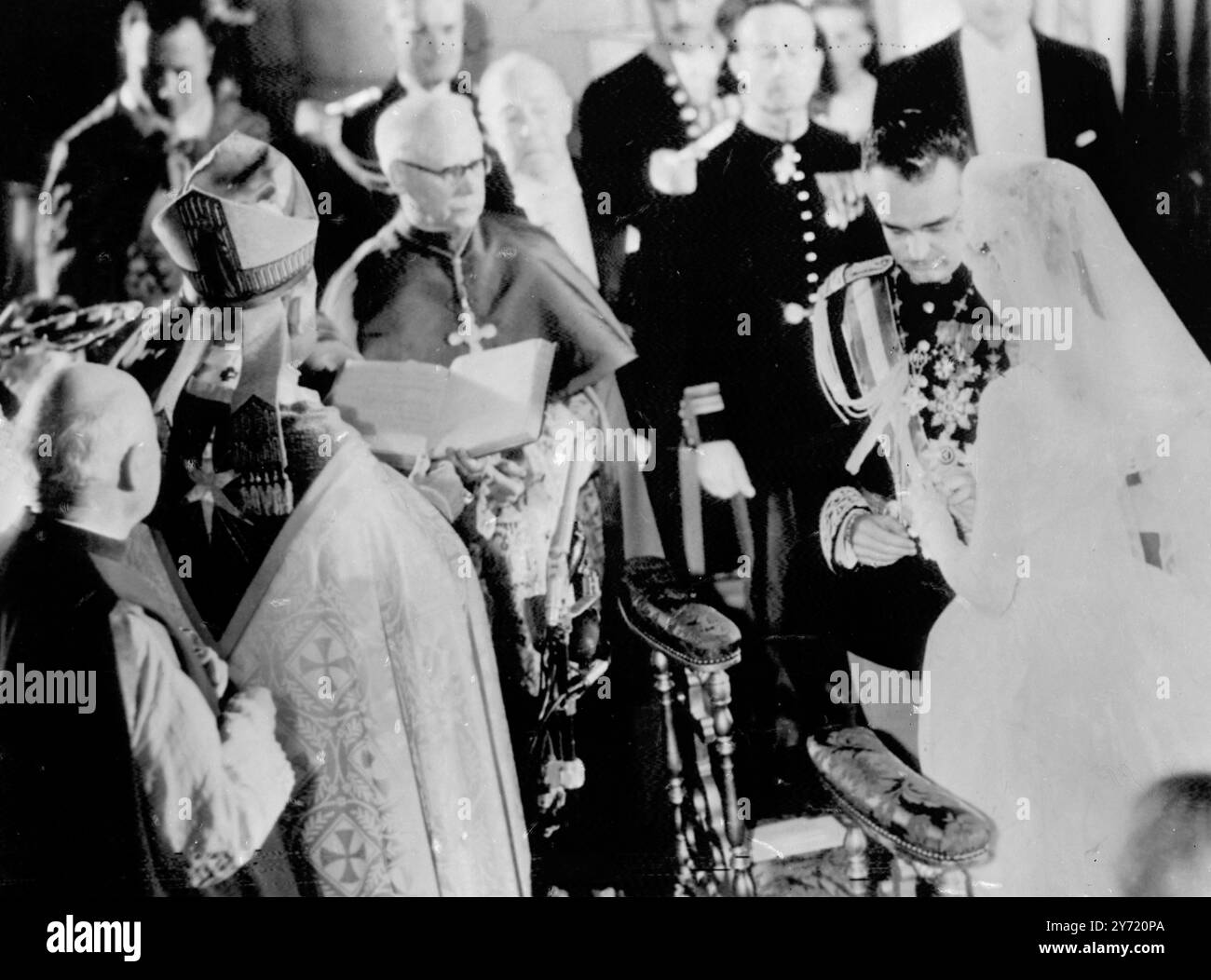 Grace supera il ring Snag durante le nozze della Cattedrale Monaco : l'Arcivescovo guarda mentre il Principe Ranieri mette l'anello al dito di Grace Kelly, durante la cerimonia religiosa di nozze nella Cattedrale di Monaco. Il Principe ha difficoltà a mettere l'anello al dito della sposa e lei lo ha aiutato con discrezione. La coppia si è sposata ieri durante una cerimonia civile. 19 aprile 1956 19 aprile 1956 Foto Stock
