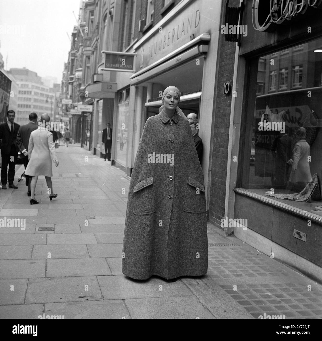 La modella Suzy si trova a pochi passi dalla Christian Dior - London Fashion House in Conduit Street, in un mantello senza maniche, lunghezza del pavimento, in tweed grigio. Pochi istanti dopo ha smontato i cinque bottoni sagomati per rivelare una gonna in patchwork in tweed grigio e una blusa in chiffon a pieghe da indossare a casa. il mantello , la gonna e la camicetta sono della nuova collezione Autunno 1969 di Christian Dior - Londra . La collezione è stata degnata da Jorn Langberg . 9 settembre 1969 Foto Stock