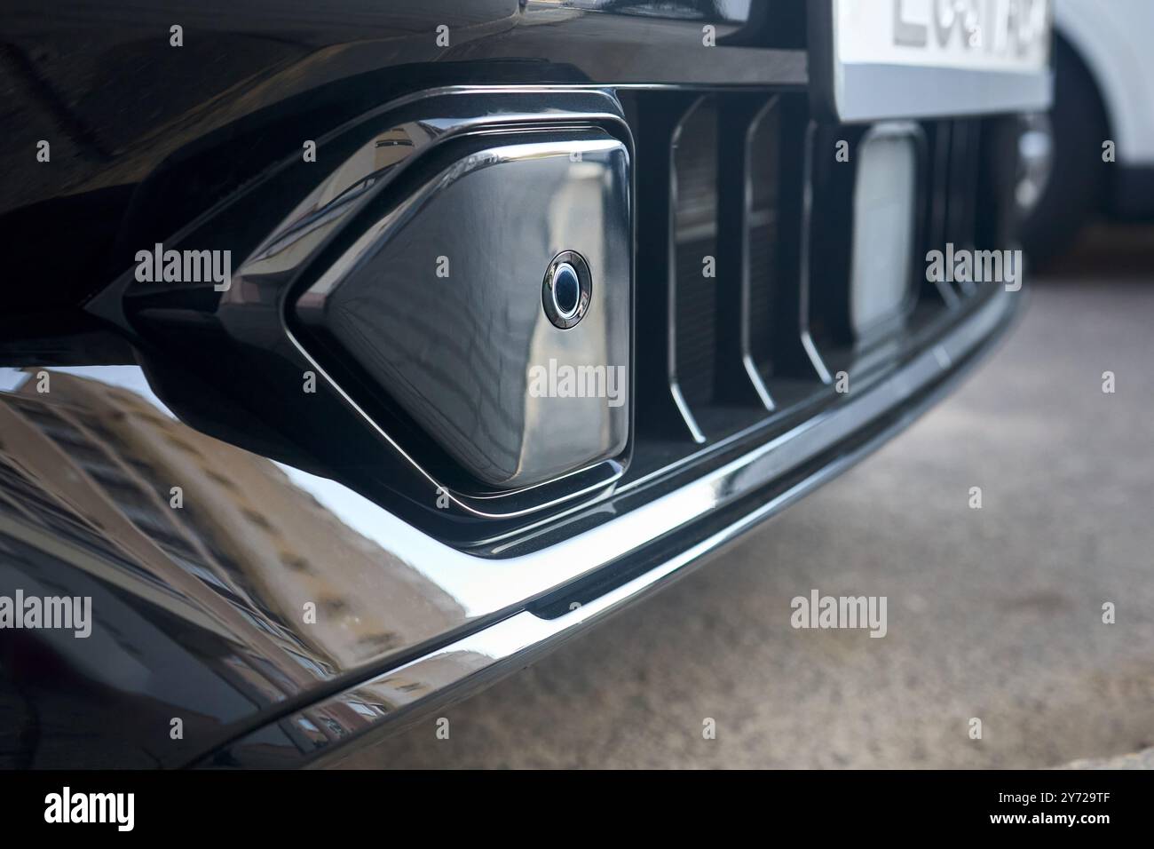 Attenzione selettiva sul lato destro dell'elemento decorativo del paraurti anteriore sensore di parcheggio del primo piano del paraurti dell'auto di lusso con sfondo a griglia con spazio imbottito Foto Stock