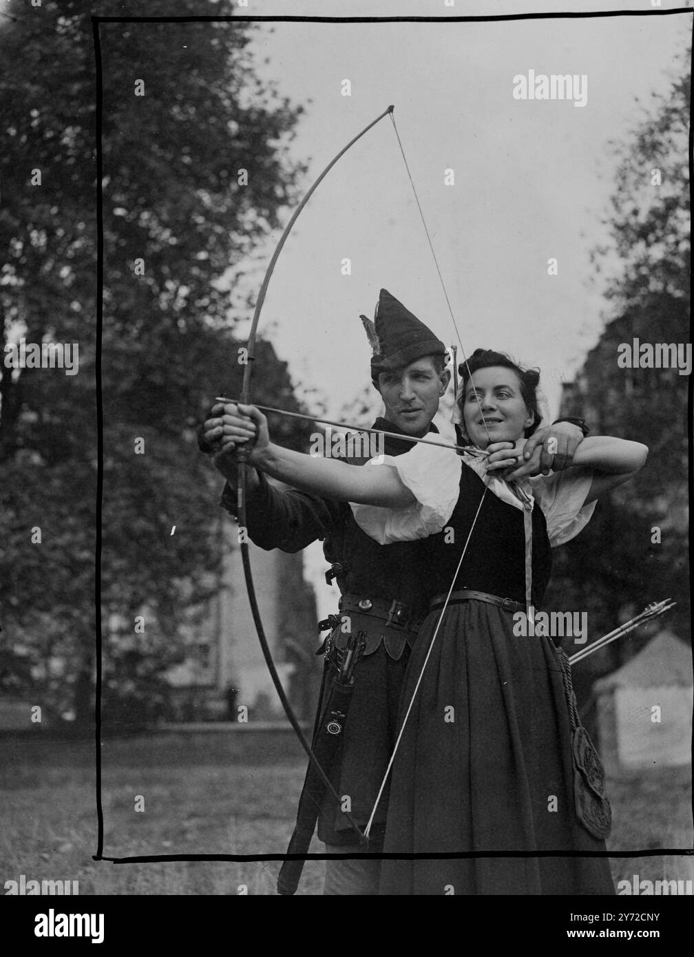 Un episodio della vita di Robin Hood e dei suoi uomini allegri era una caratteristica del terzo show annuale di Chelsea, tenuto oggi al Burton's Court Grounds, Chelsea, Londra. Gli "Men in Lincoln Green" erano membri del Royal Toxophilite Club, che dava dimostrazioni sia con archi e frecce in legno del vecchio tempo, sia con quelli più moderni, precisi e lunghi in acciaio a spirale. Le immagini mostrano: La cameriera Marion (Miss Catherine Rogers), riceve istruzioni sull'uso del lungo arco da Robin Hood (Mr Tom Weston) allo spettacolo di Chelsea. 27 settembre 1947 Foto Stock