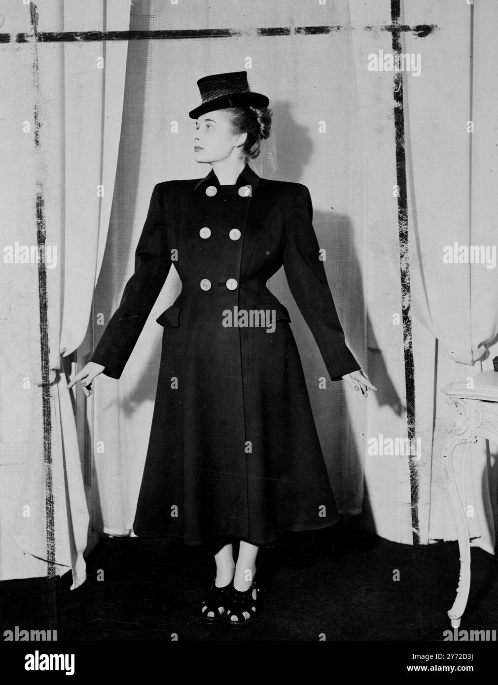 Lo stile coachman è il tema di questo ensemble, uno degli ultimi ad essere mostrato a Londra dalla casa di moda di Julian Sayers. Presenta un cappotto in tessuto rosso per il viso, accuratamente sartoriale con fianchi imbottiti e gonna svasata. I bottoni dorati e il colletto in basso dai toni alti sottolineano il design. Il cappello è dello stesso stile, decorato con la corona e lungo la schiena con la rete. Poco più di due anni fa Julian Sayers stava combattendo con i commando francesi liberi. Ha iniziato la sua carriera nella progettazione di abiti con un importante Budapest Couturier, e in seguito ha lavorato in alcune delle principali case di moda di Foto Stock