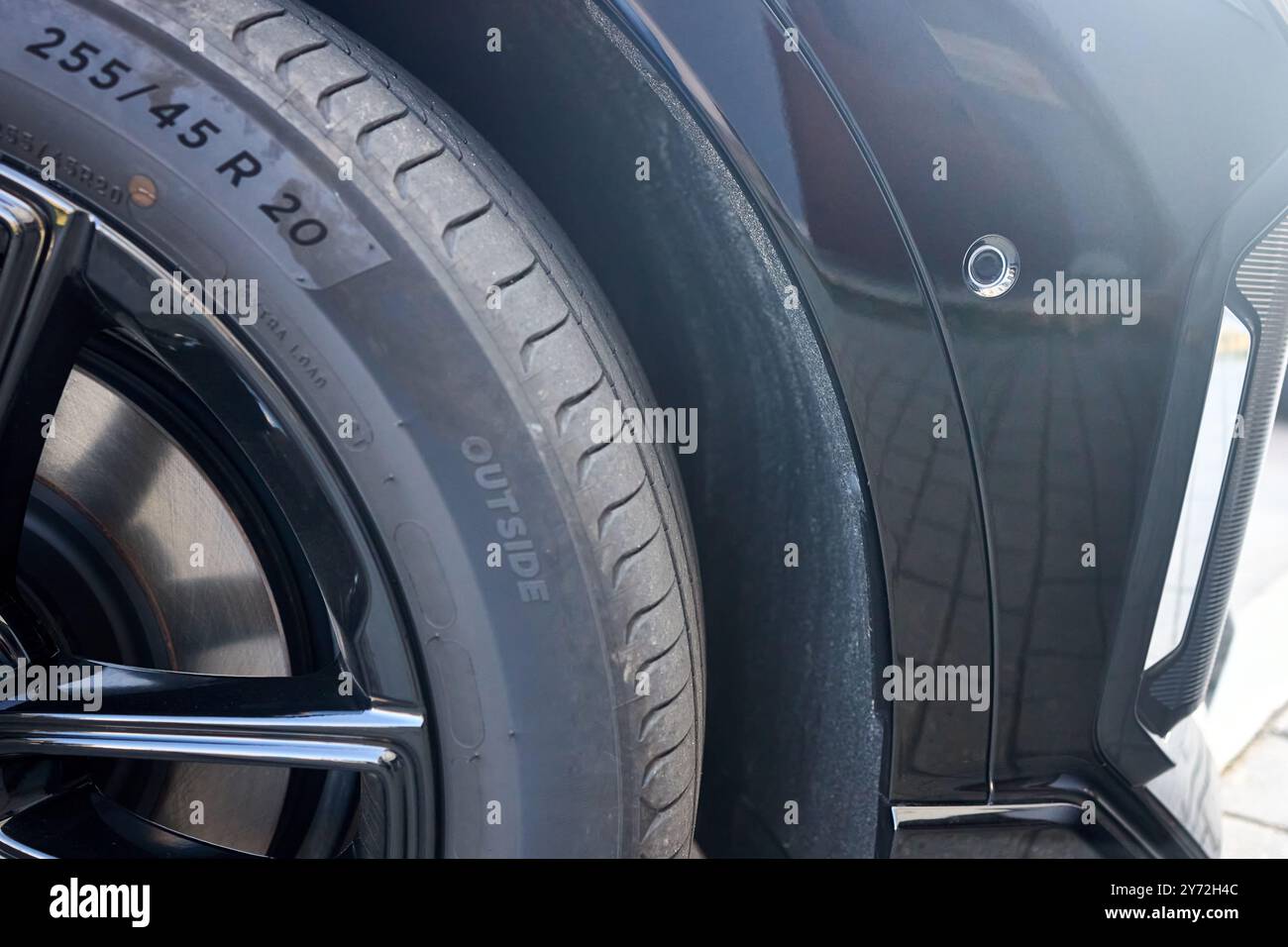 Attenzione selettiva sul lato destro dell'elemento decorativo del paraurti anteriore sensore di parcheggio laterale del primo piano del paraurti dell'auto di lusso con ruota R20 e cerchione in lega Foto Stock
