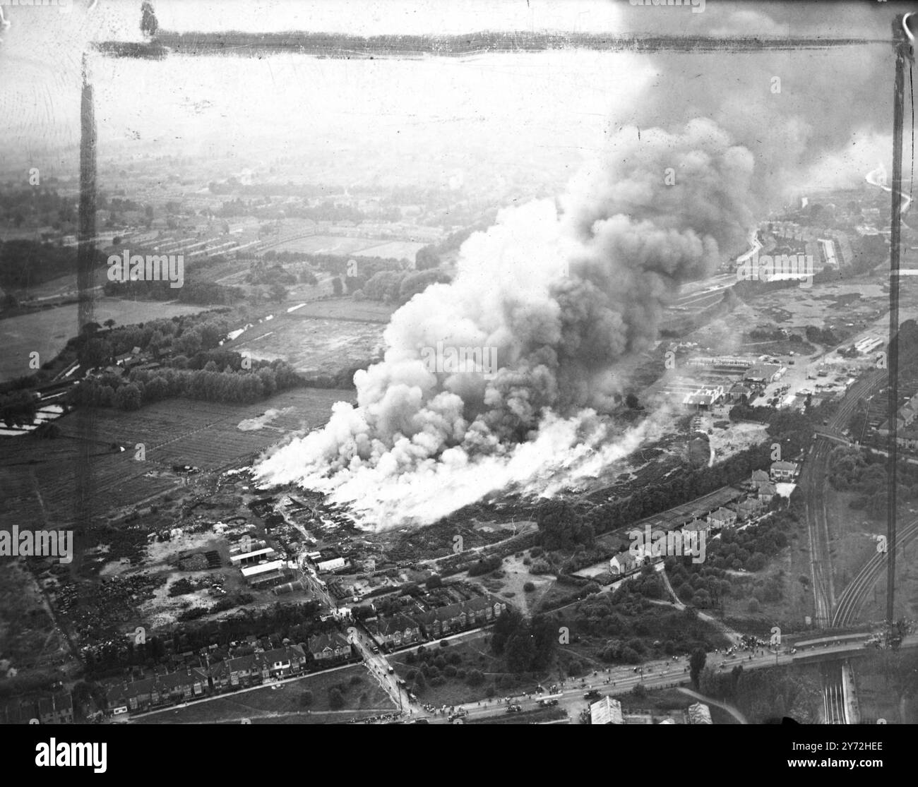 Una vista aerea di un'enorme folla di fumo viola-nero soffiato fuori il sole da Londra sud e centro questa sera (lunedì), i vigili del fuoco provenienti da tutti i sobborghi sud hanno combattuto un feroce incendio nella più grande discarica di gomma di Londra, a Carshalton Road, Mitcham Junction. Migliaia di tonnellate di rottami di gomma bruciarono rapidamente mentre i vigili del fuoco lottarono per far giocare l'acqua sul fuoco. La mancanza di acqua ha gravemente ostacolato gli sforzi per sottomettere le fiamme. Si dice che una fabbrica vicina sia stata accesa, e bande di uomini lavorano per cancellare una "rottura" della scena la discarica e le case vicine. L'incendio ha fornito il più spettacolare Foto Stock