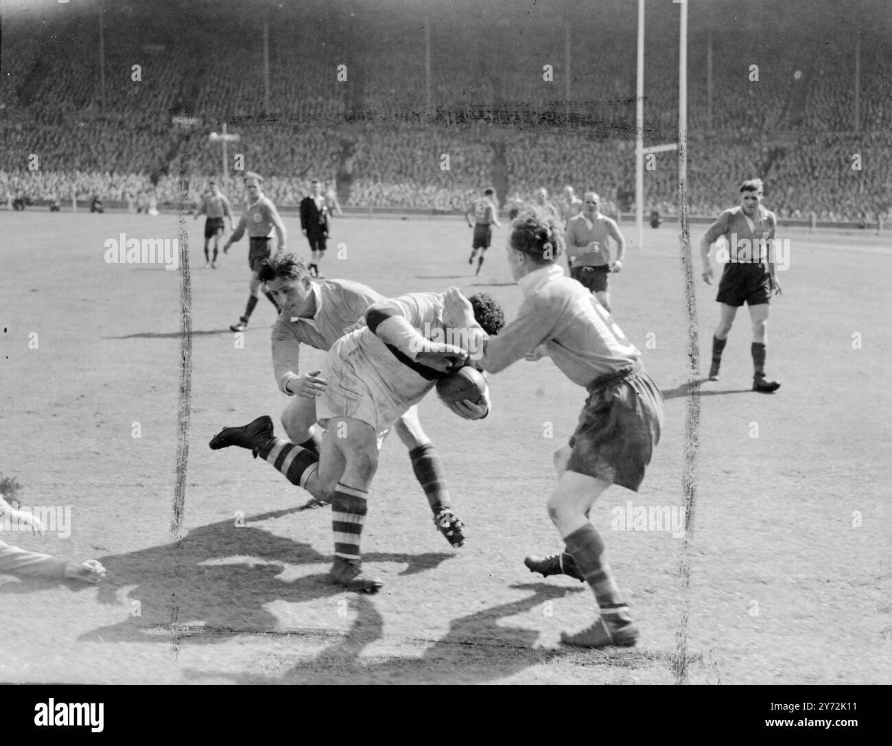 Royalty ha partecipato al Rugby Union Match al Wembley Stadium, per la prima volta quando il Leeds ha incontrato Bradford Northern nella finale di Coppa di rugby a 13. Il Duca e la Duchessa di Gloucester si stringono la mano ai giocatori prima del calcio d'inizio, e poi guardano la partita prima di presentare la coppa alla squadra vincente. Spettacoli fotografici: Un giocatore del Bradford Northern (pantaloncini bianchi) incontra l'opposizione di due giocatori del Leeds durante la partita a Wembley. 3 maggio 1947 Foto Stock