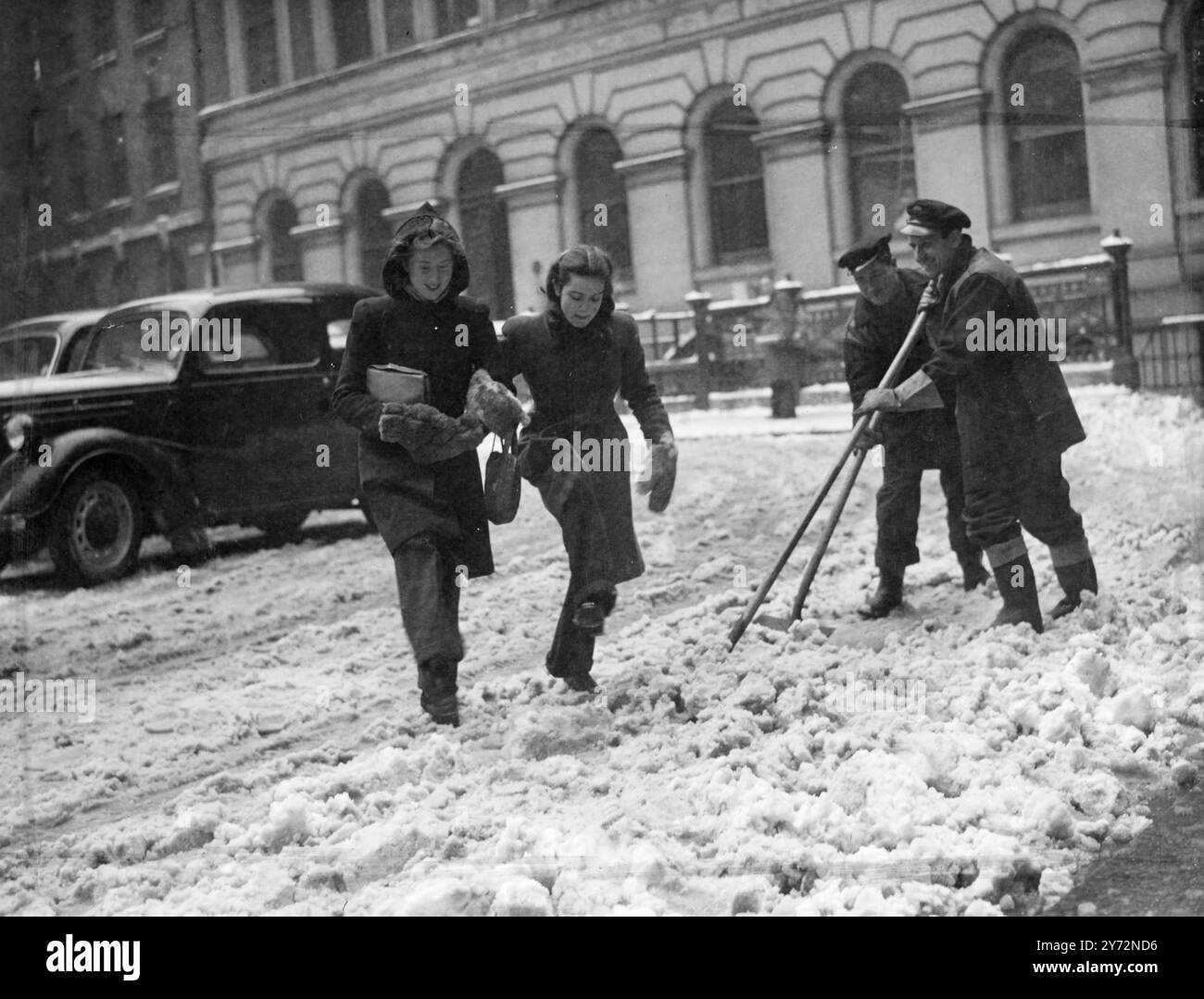 Scegli "Em Up" Girls! Queste due ragazze operaie in città, con un abbigliamento adatto per il tempo nevoso, hanno dovuto scegliere con attenzione quando hanno attraversato la strada coperta, mentre le spazzatrici della città hanno trovato lavoro per ripulire il disordine. 6 marzo 1947 Foto Stock