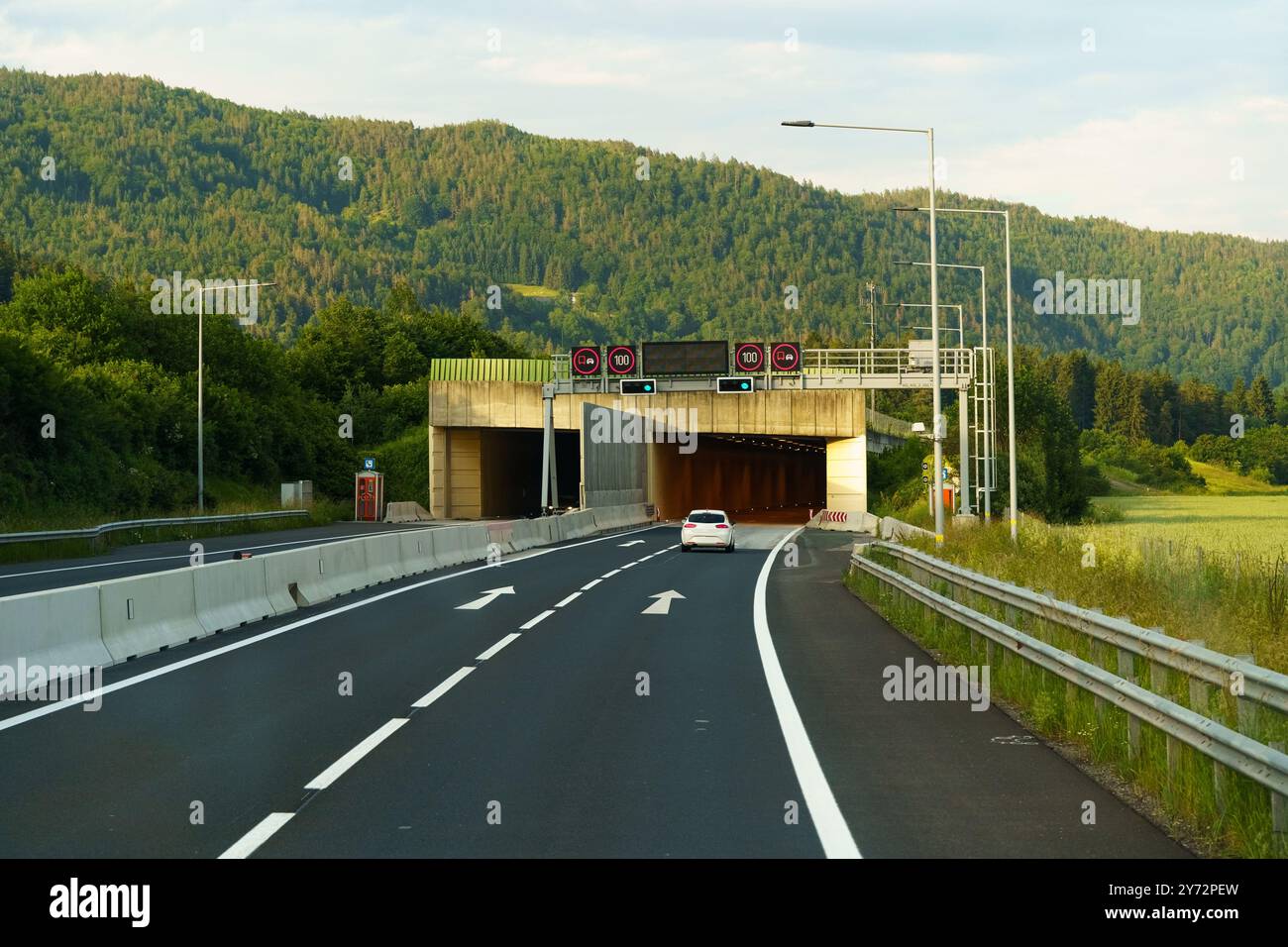 Un veicolo solitario si avvicina all'ingresso del tunnel, circondato da lussureggianti colline verdi sotto un cielo blu brillante, invitando un tranquillo viaggio avanti su una af soleggiata Foto Stock